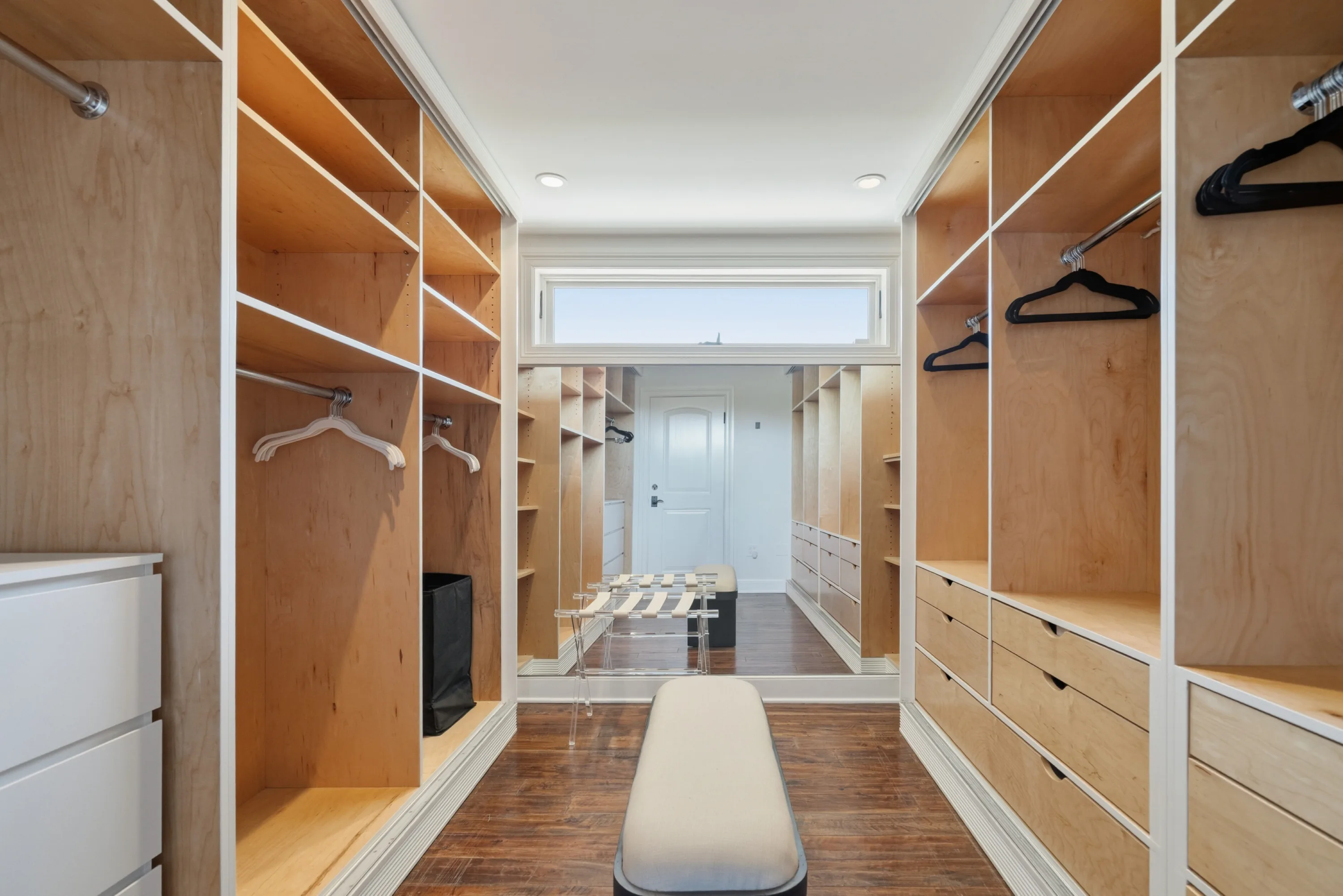 Walk-through wardrobe lined with open timber shelving, hanging rails and a padded bench