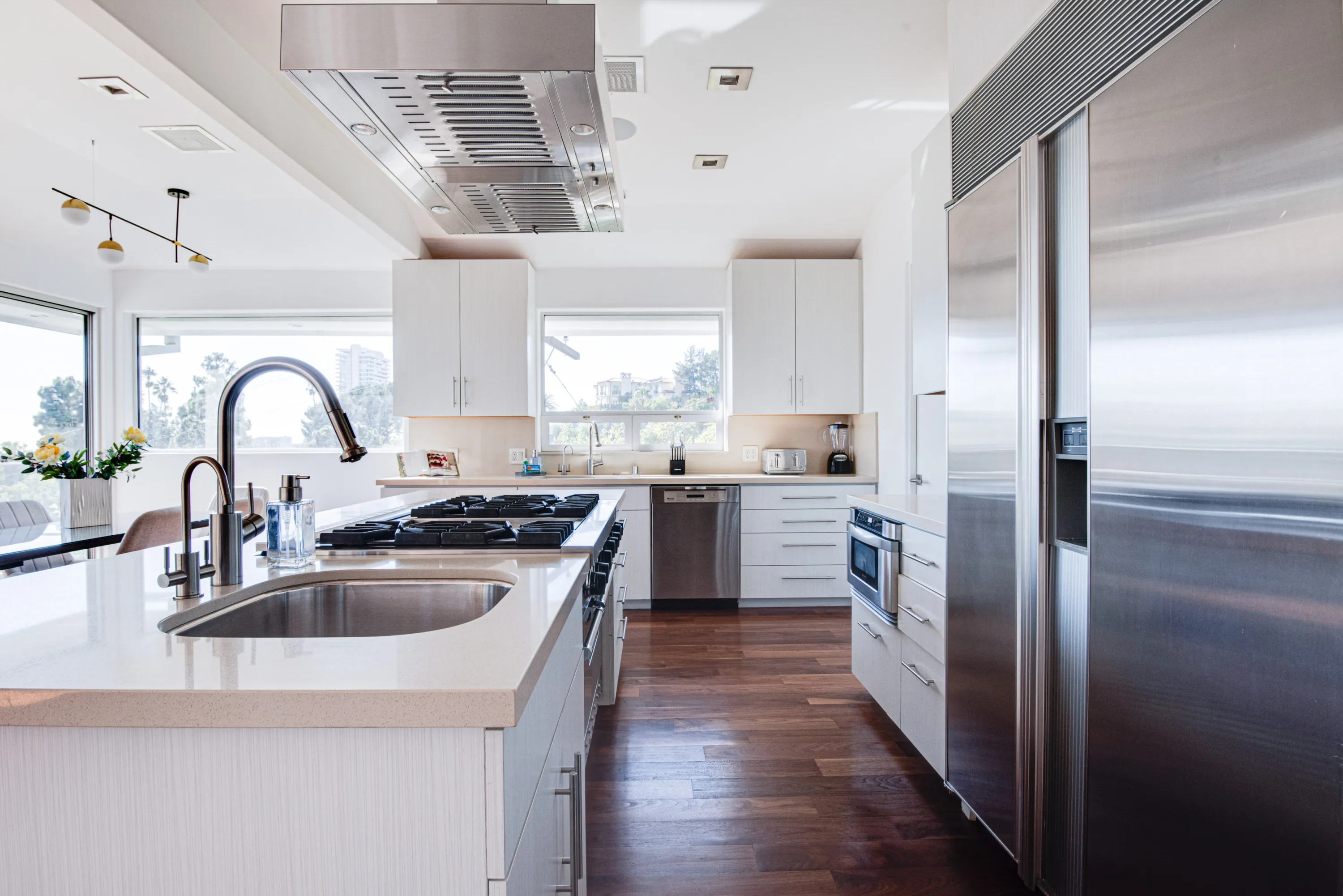 Chef's kitchen with long quartz island, gas range under a steel hood and walnut floors, windows framing treetops