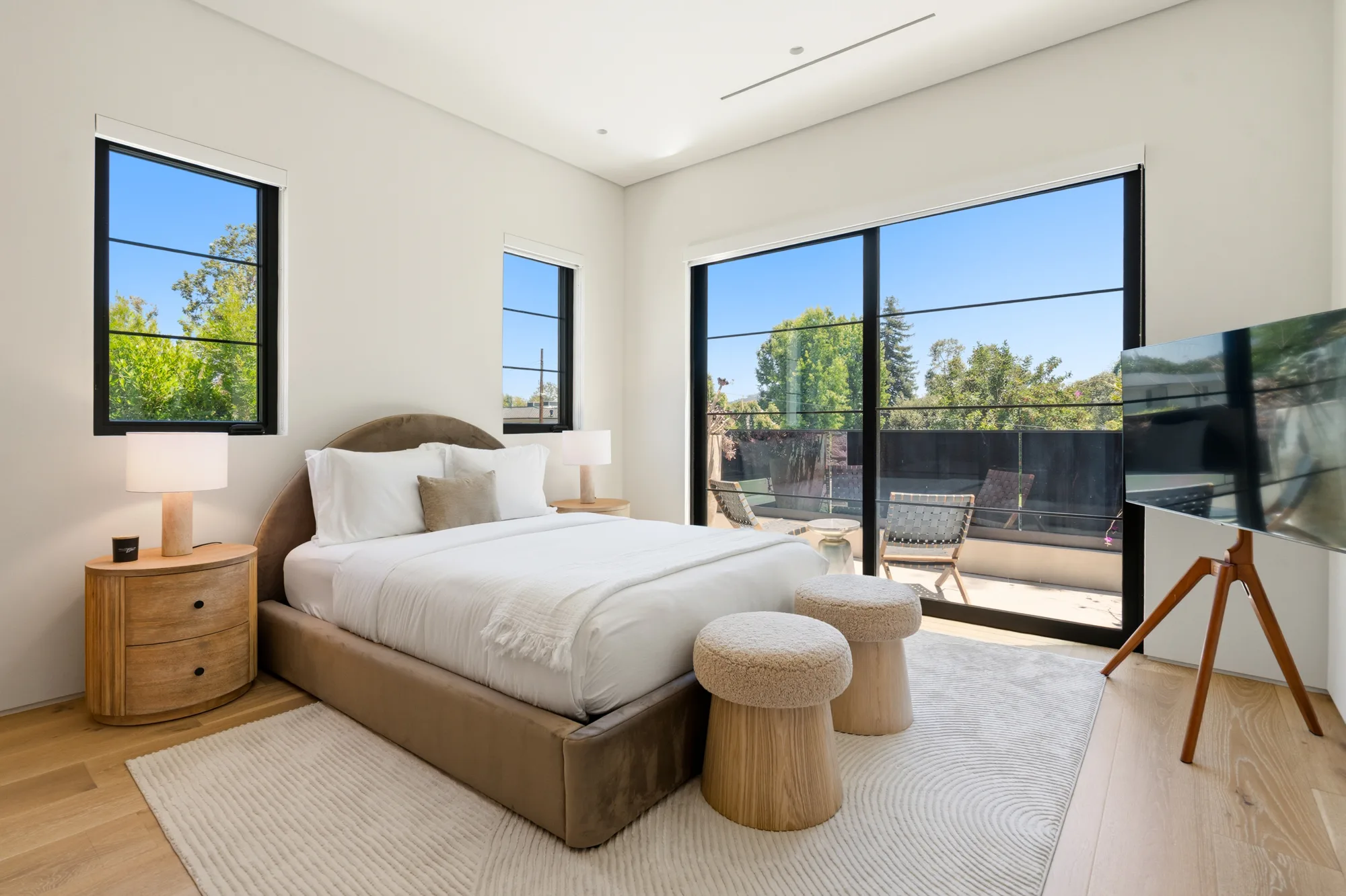 Upper bedroom opening to a private terrace, velvet headboard, twin boucle stools and swivel-mounted TV