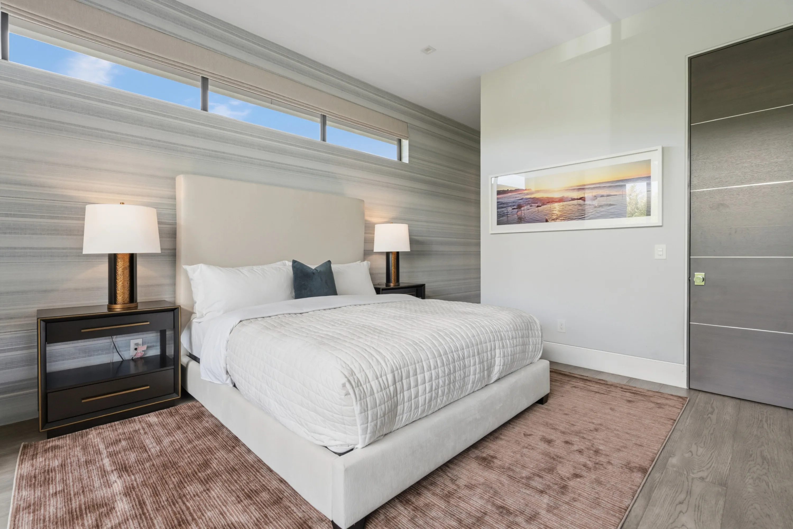 Second view of the same guest room, showing striated stone feature wall and framed coastal sunset print