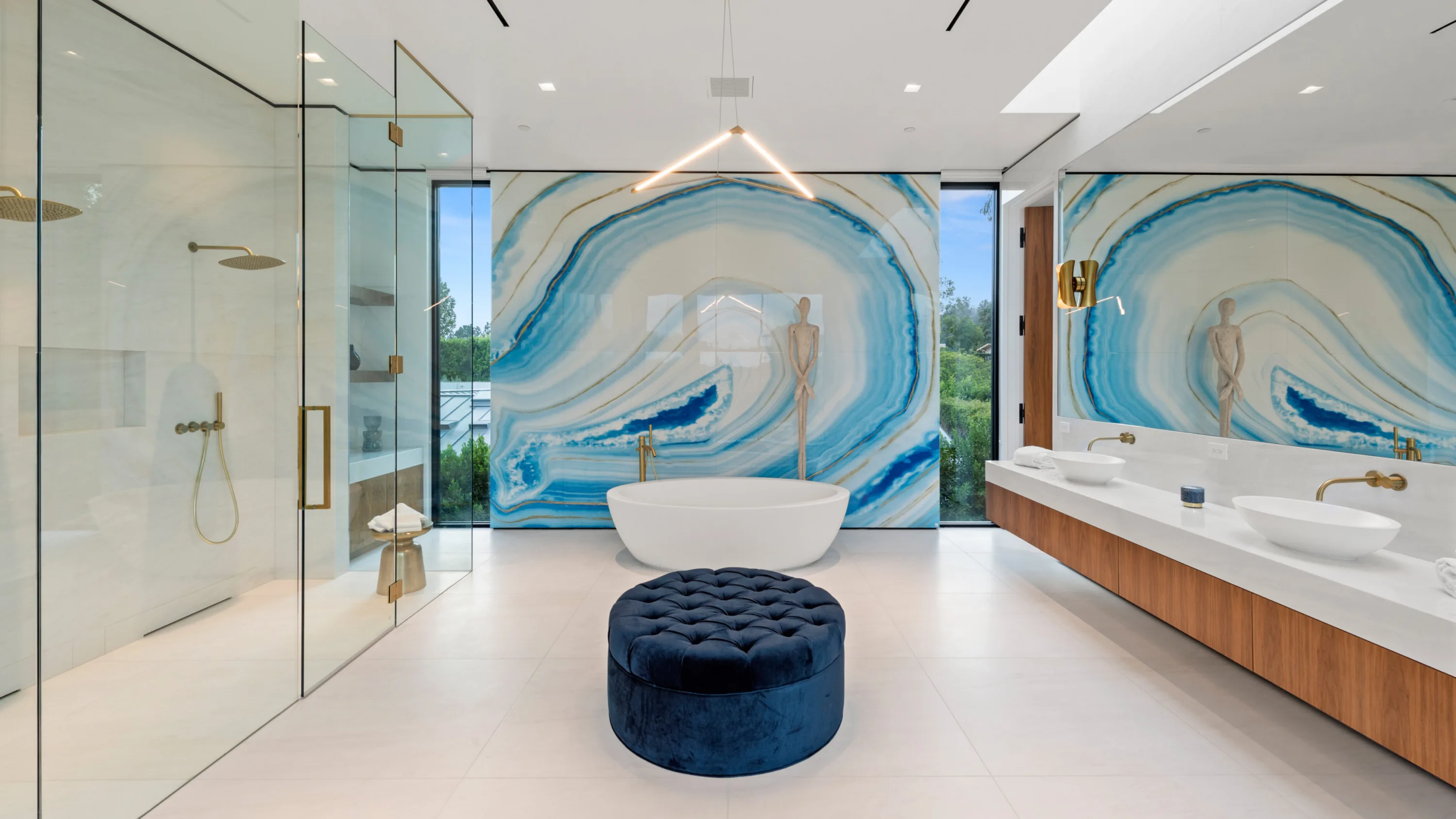 Primary bath with freestanding tub against a blue agate slab wall, walk-in glass shower and velvet round ottoman