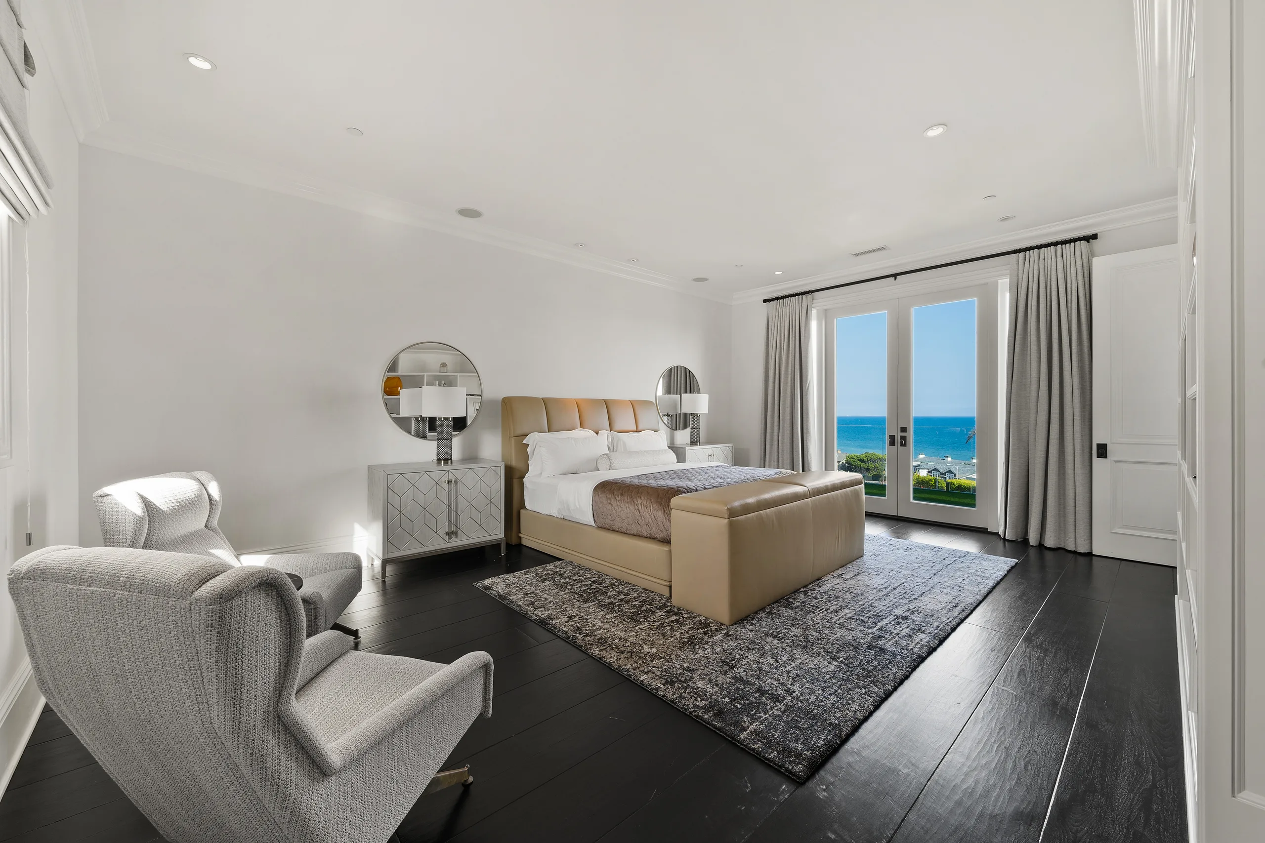 Ocean-facing bedroom with leather-upholstered bed, wing chairs and French doors opening to the blue horizon