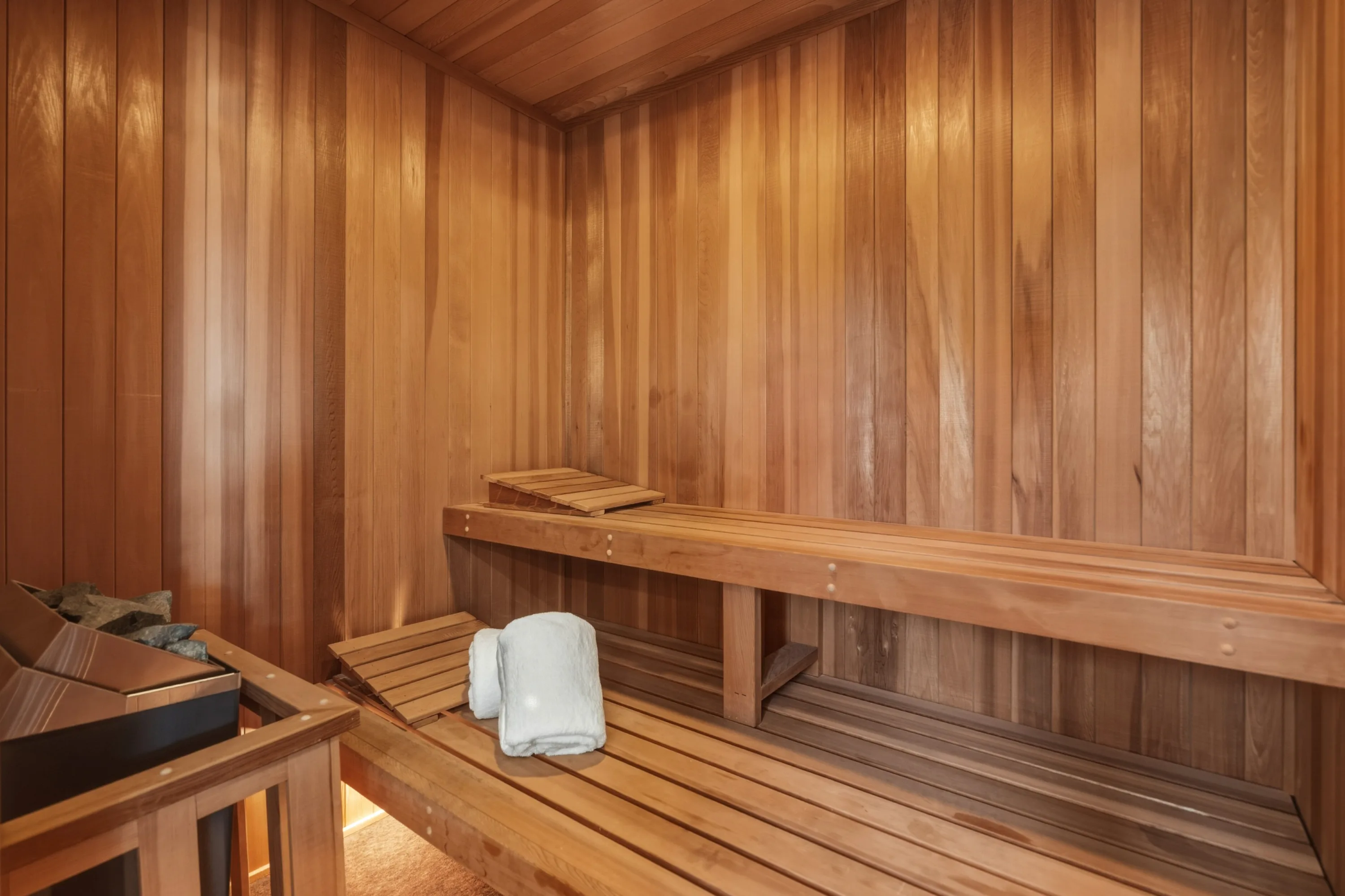 Cedar-lined sauna with two-tier benches, heater stones and a rolled white towel