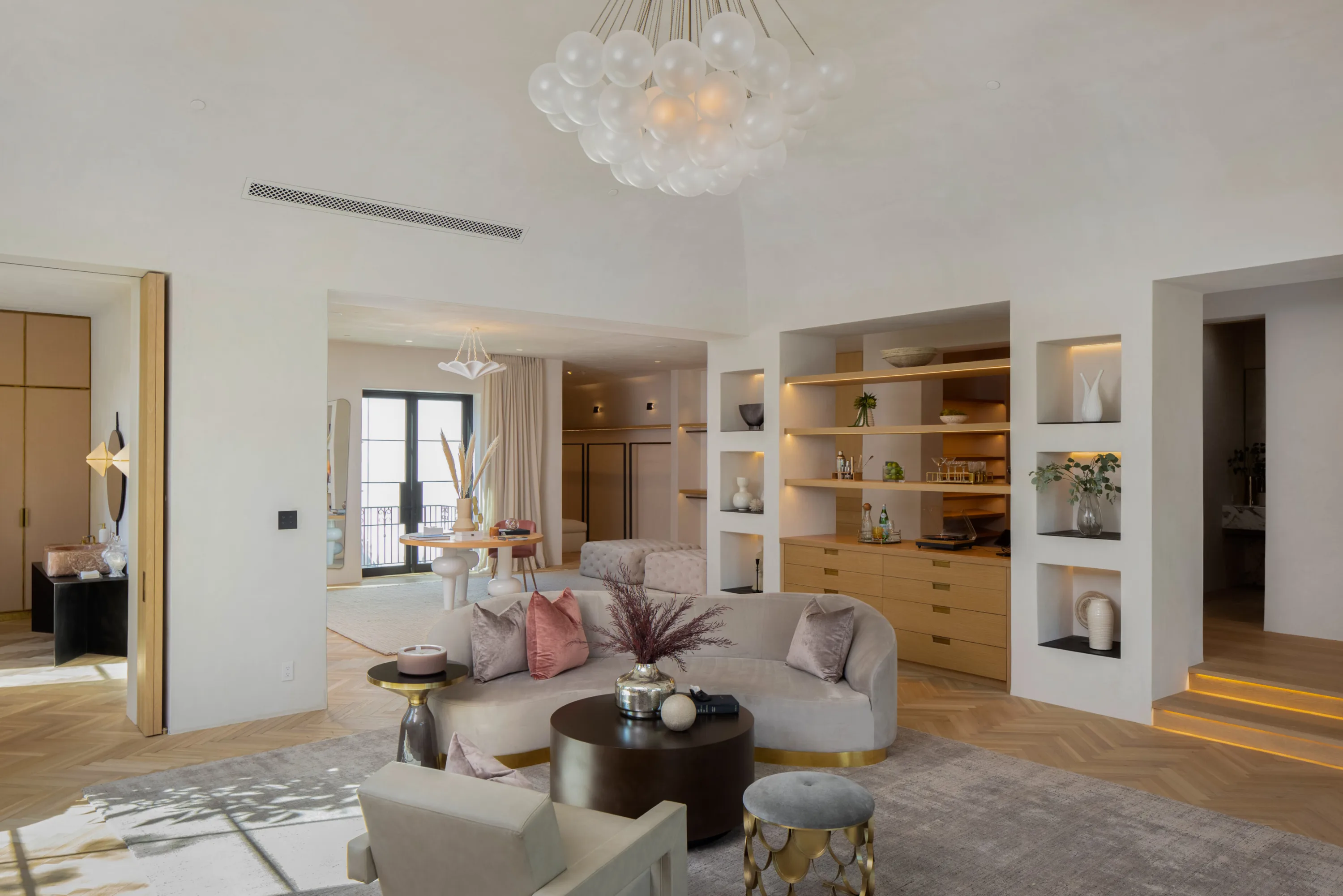 Curved sofa and lit display niches in the suite's lounge beneath a cluster-glass pendant