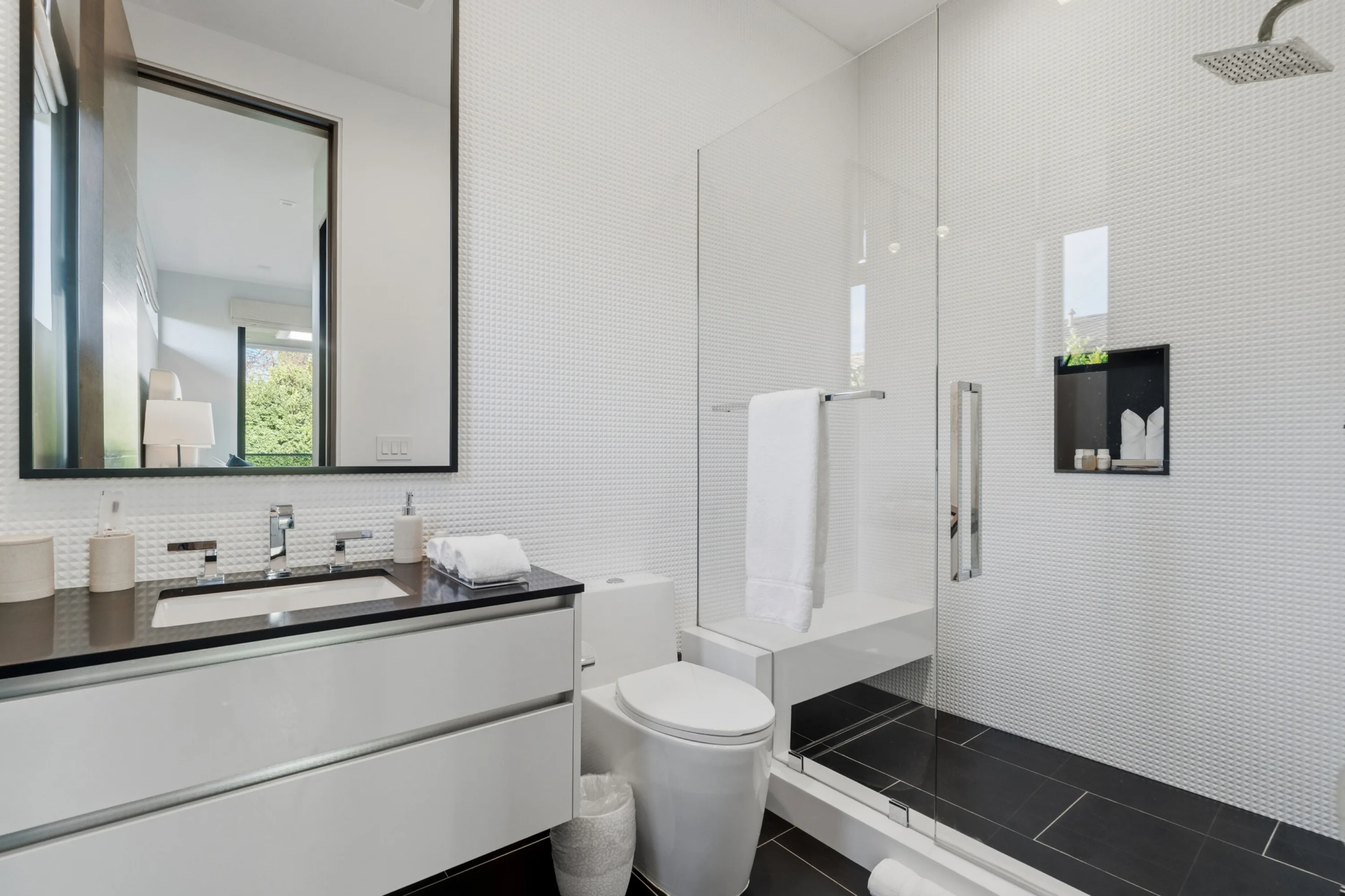 Guest en suite in white mosaic tile with glass walk-in shower, bench seat and black stone vanity
