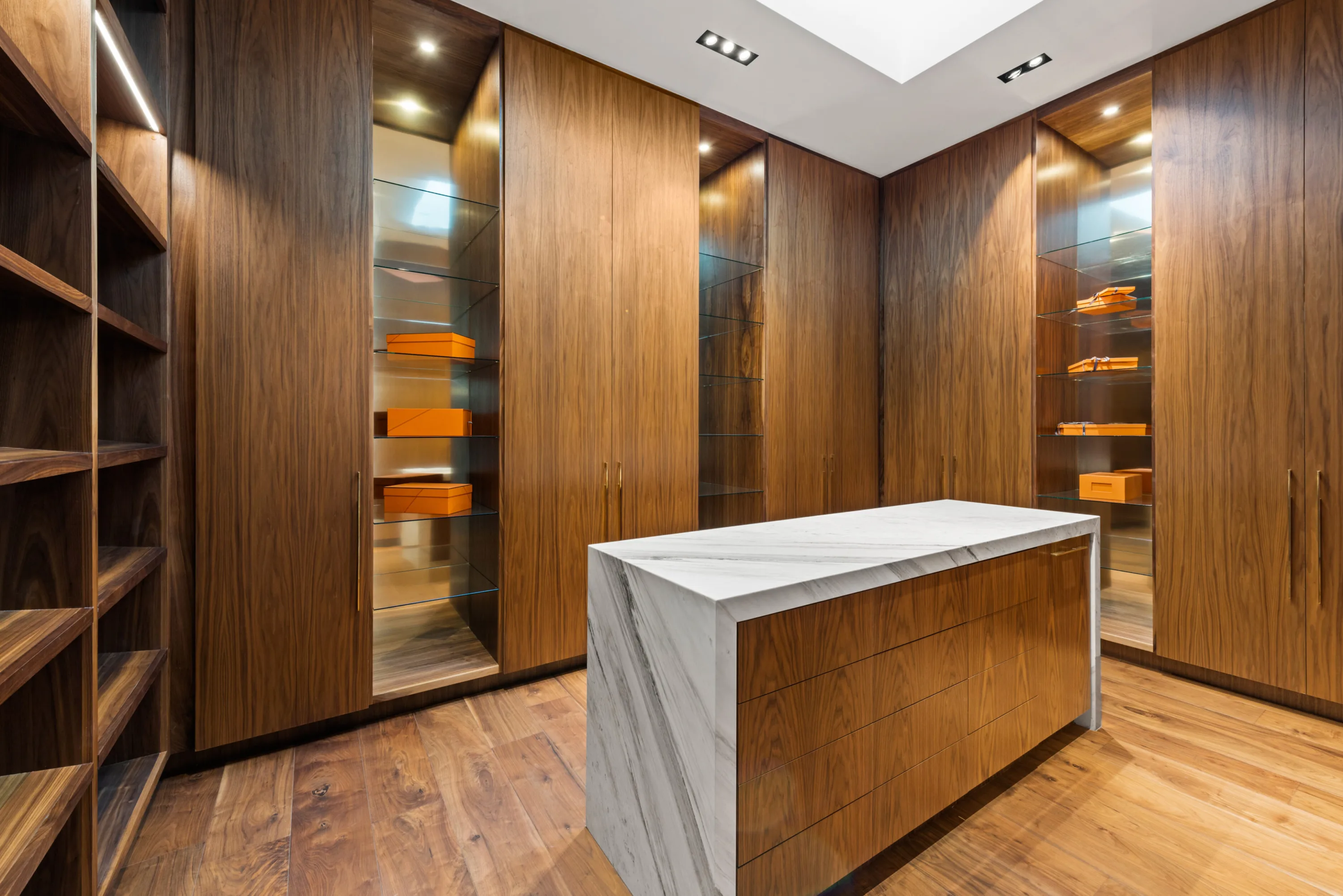 Walnut-panelled dressing room with lit glass display niches and a marble-wrapped island of drawers