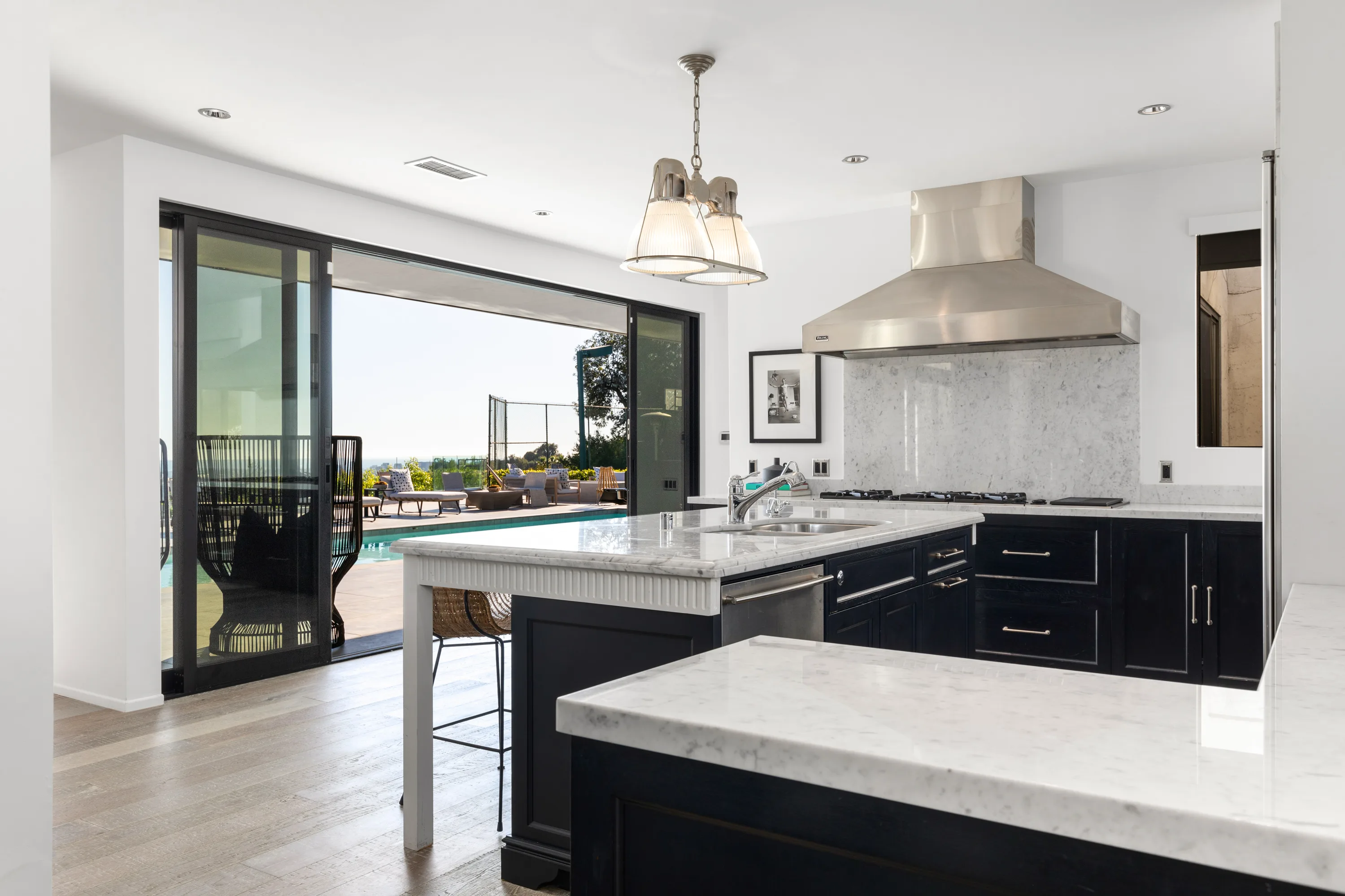 Chef's kitchen in marble and inky cabinetry, sliding wall open to the pool deck and tennis court