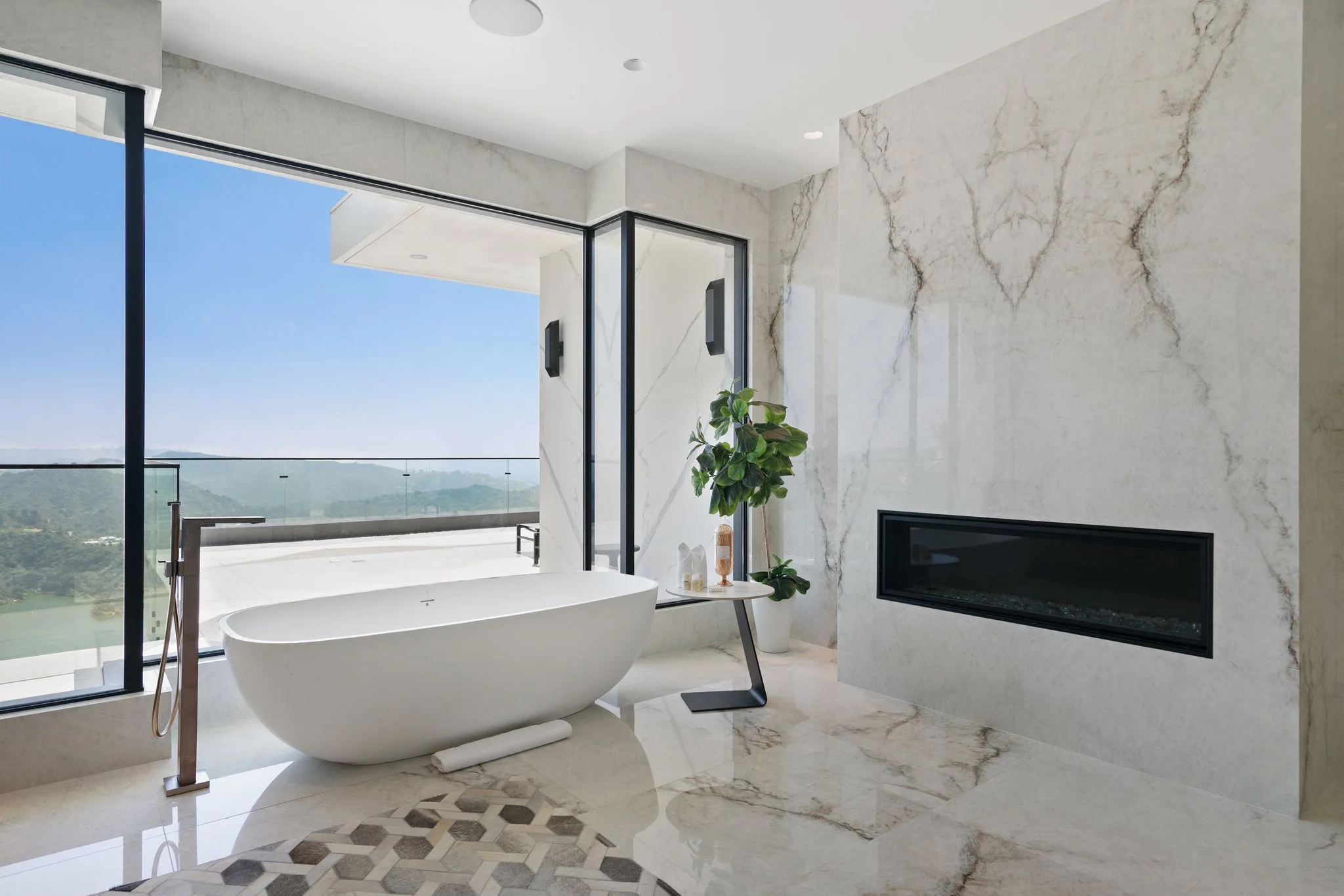 Sculptural soaking tub at the window with reservoir and canyon views, beside a marble fireplace wall