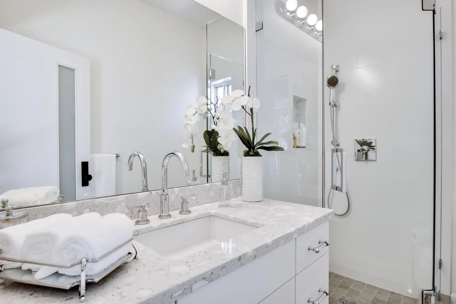 Guest bathroom vanity in quartz with rolled towels, orchids and a glass-enclosed shower alongside
