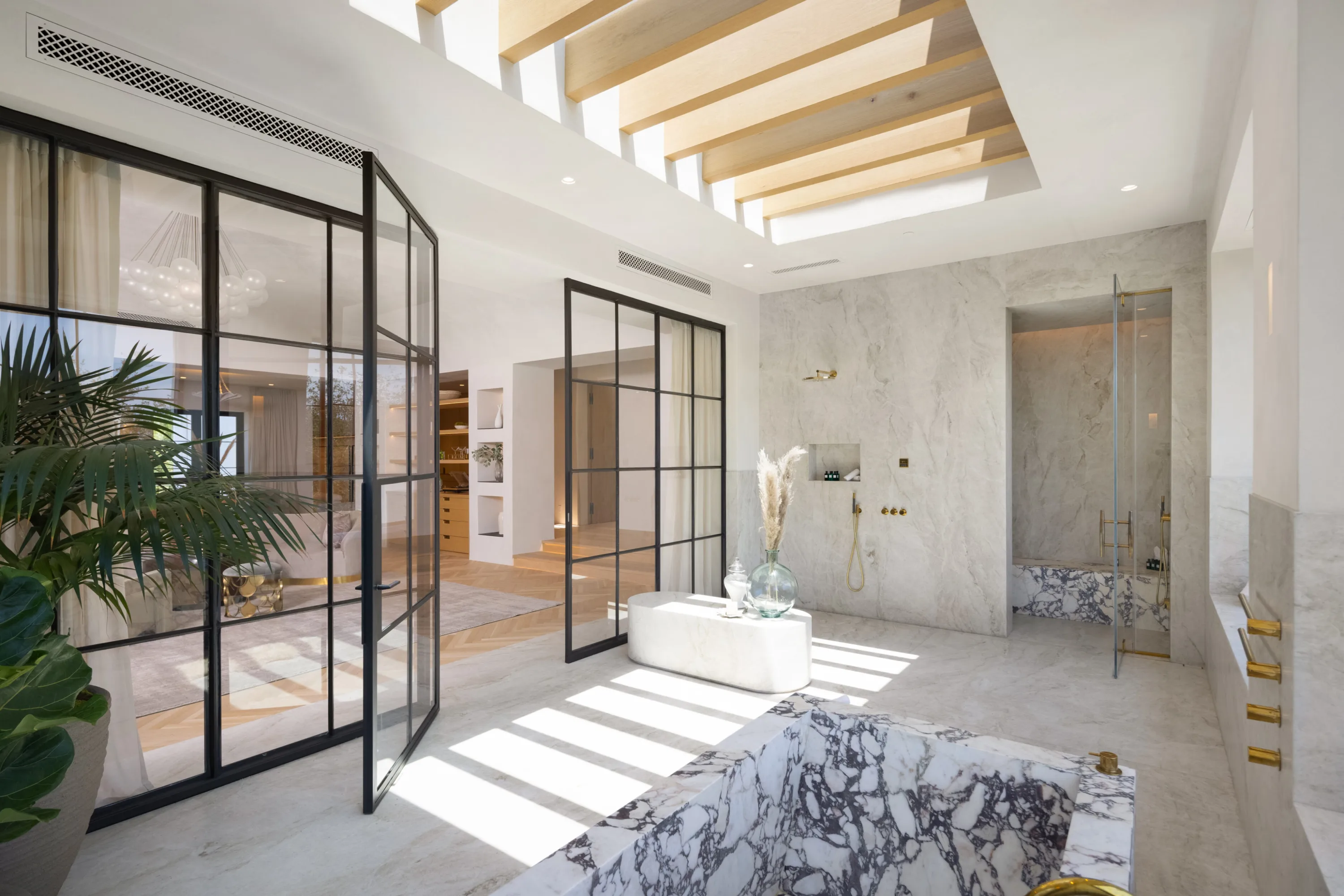 Skylit primary bath with marble soaking tub, walk-in shower and black steel glass partitions