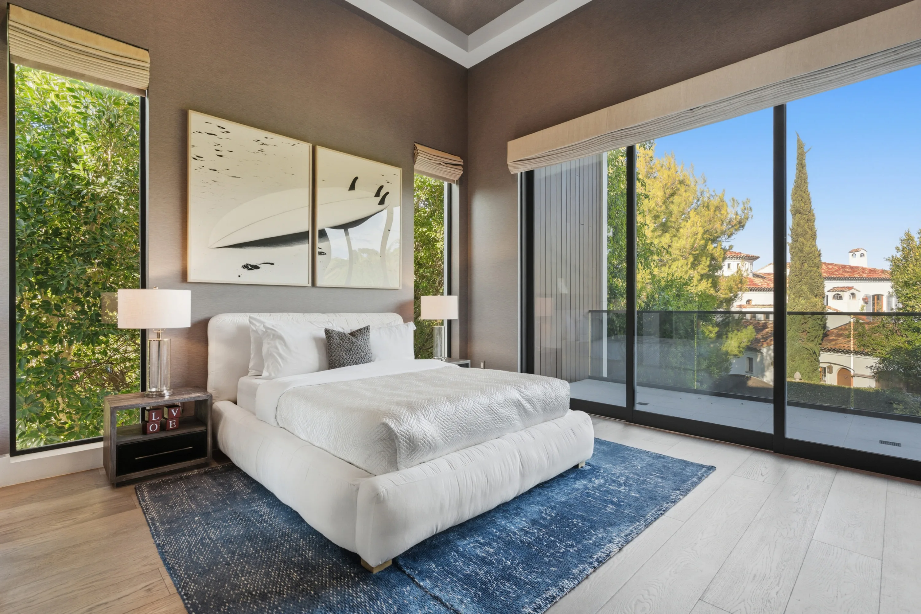 Bedroom in taupe with surfboard diptych above the bed and floor-to-ceiling glass onto a treetop balcony