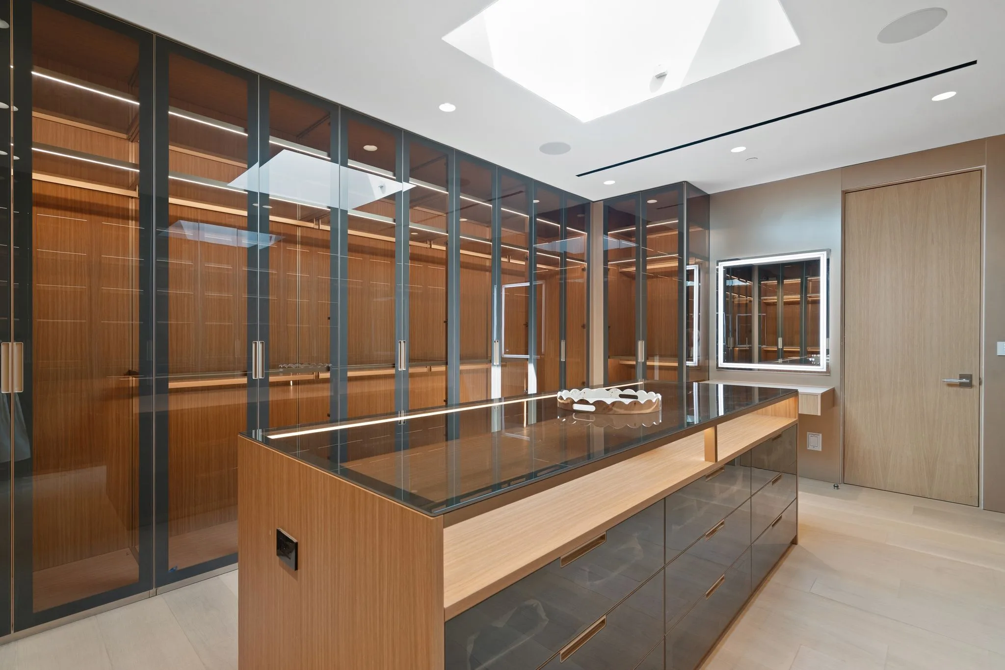 Walk-in dressing room with glass-front oak wardrobes, skylight overhead and a glass-topped display island