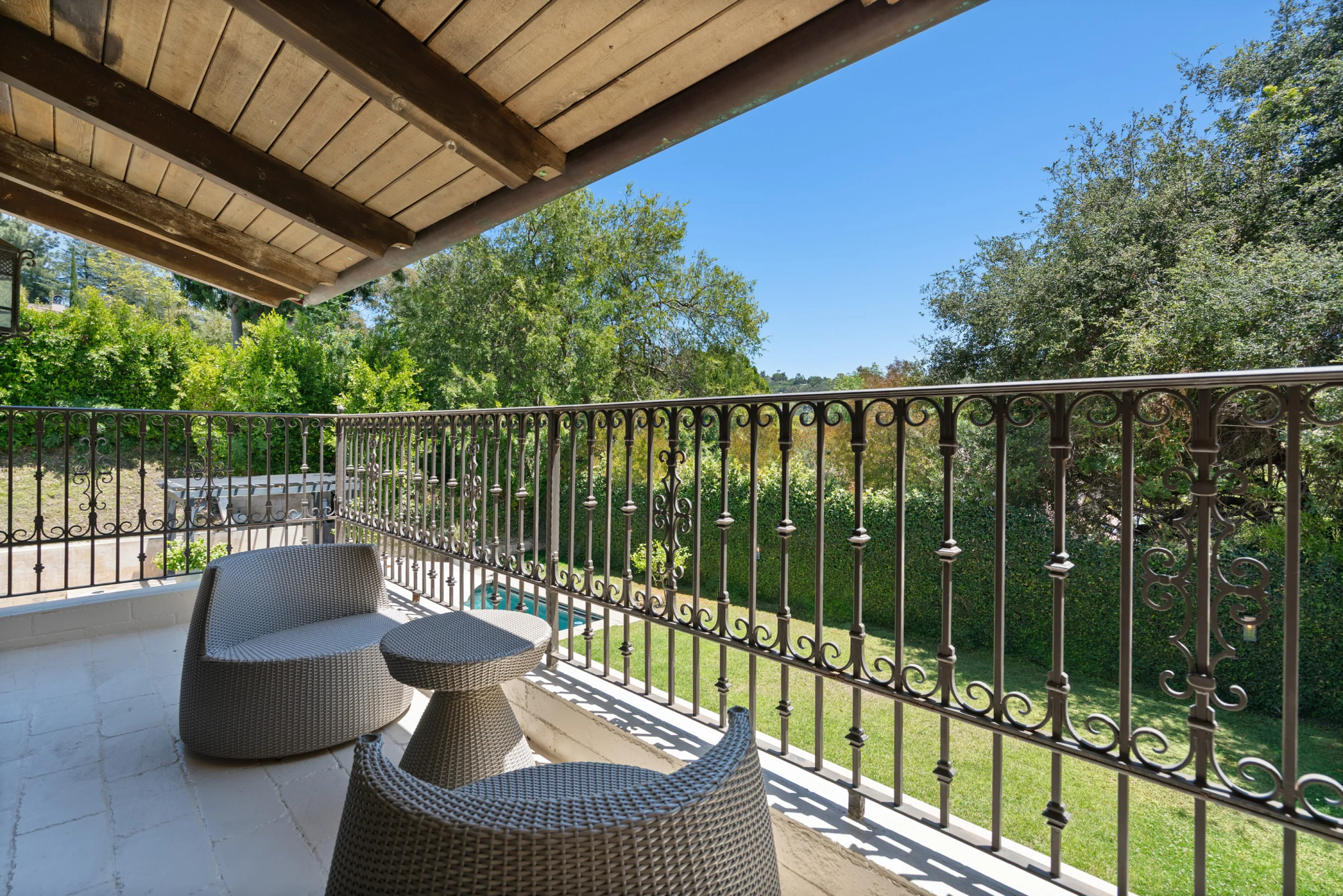 Covered balcony with woven armchairs looking down over the lawn and pool through ornate ironwork