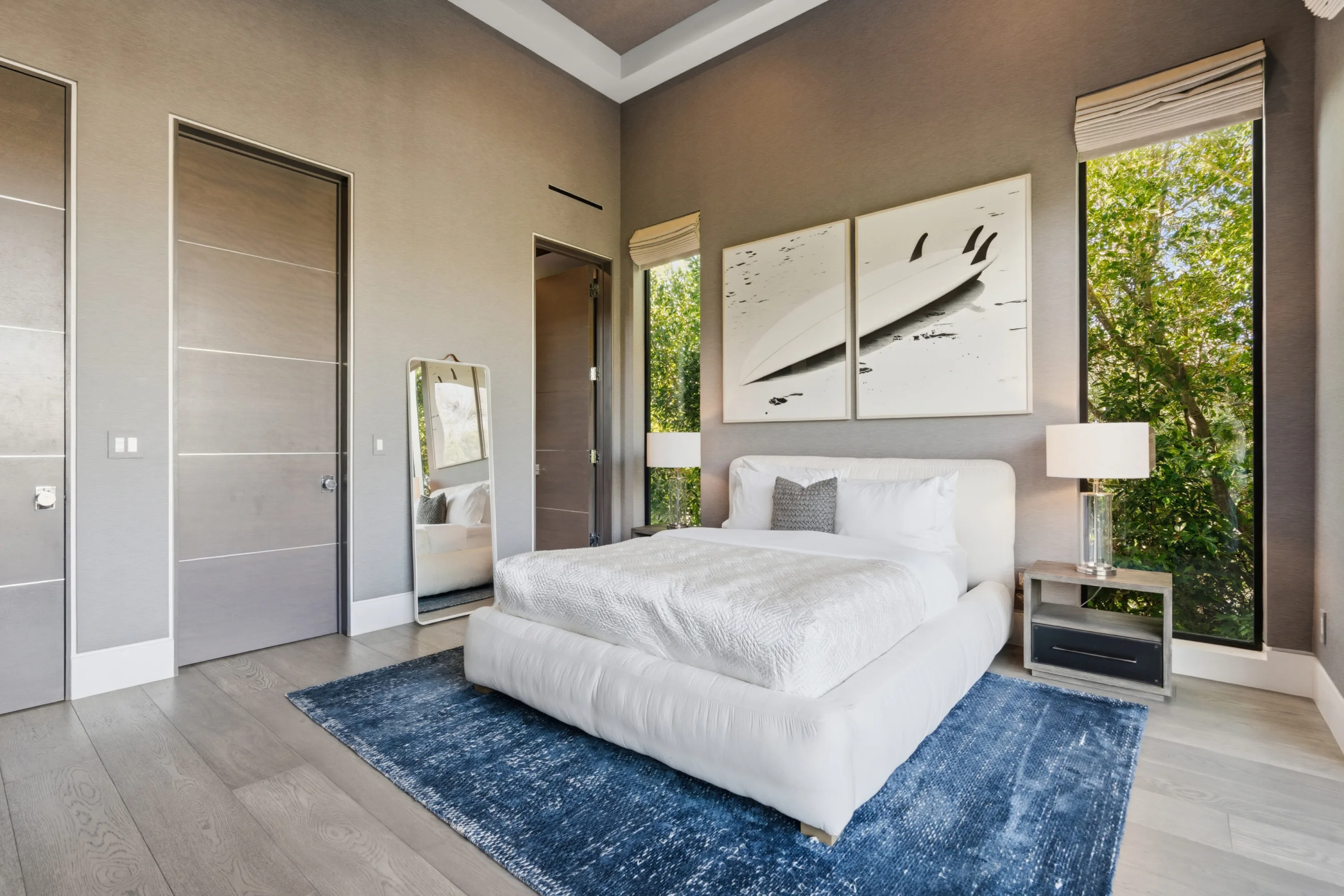 Wider angle of the surf-themed bedroom, leaning mirror and windows filled with green canopy