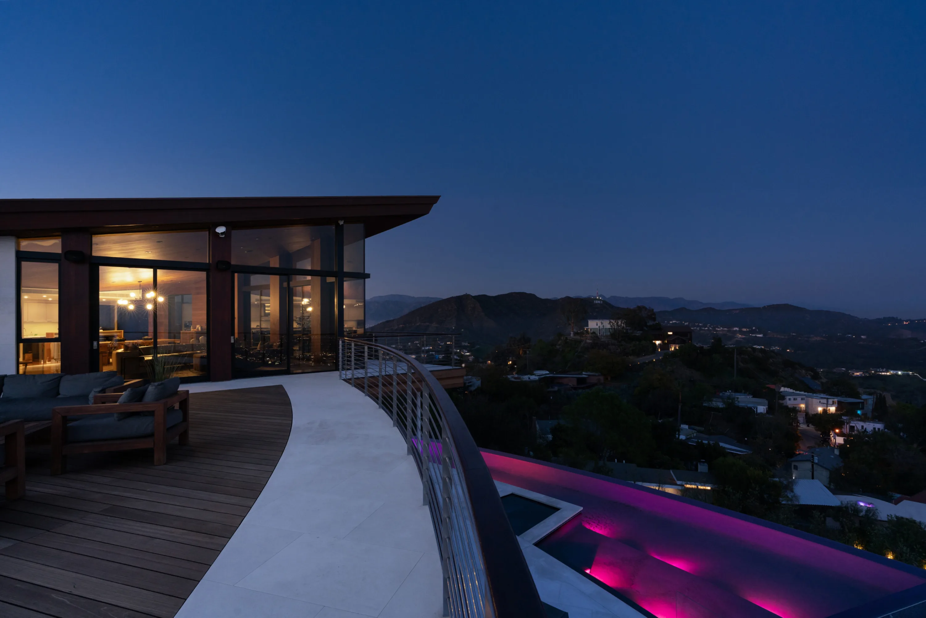 Hillside deck at blue hour with a magenta-lit pool below and canyon lights stretching to the ridgeline