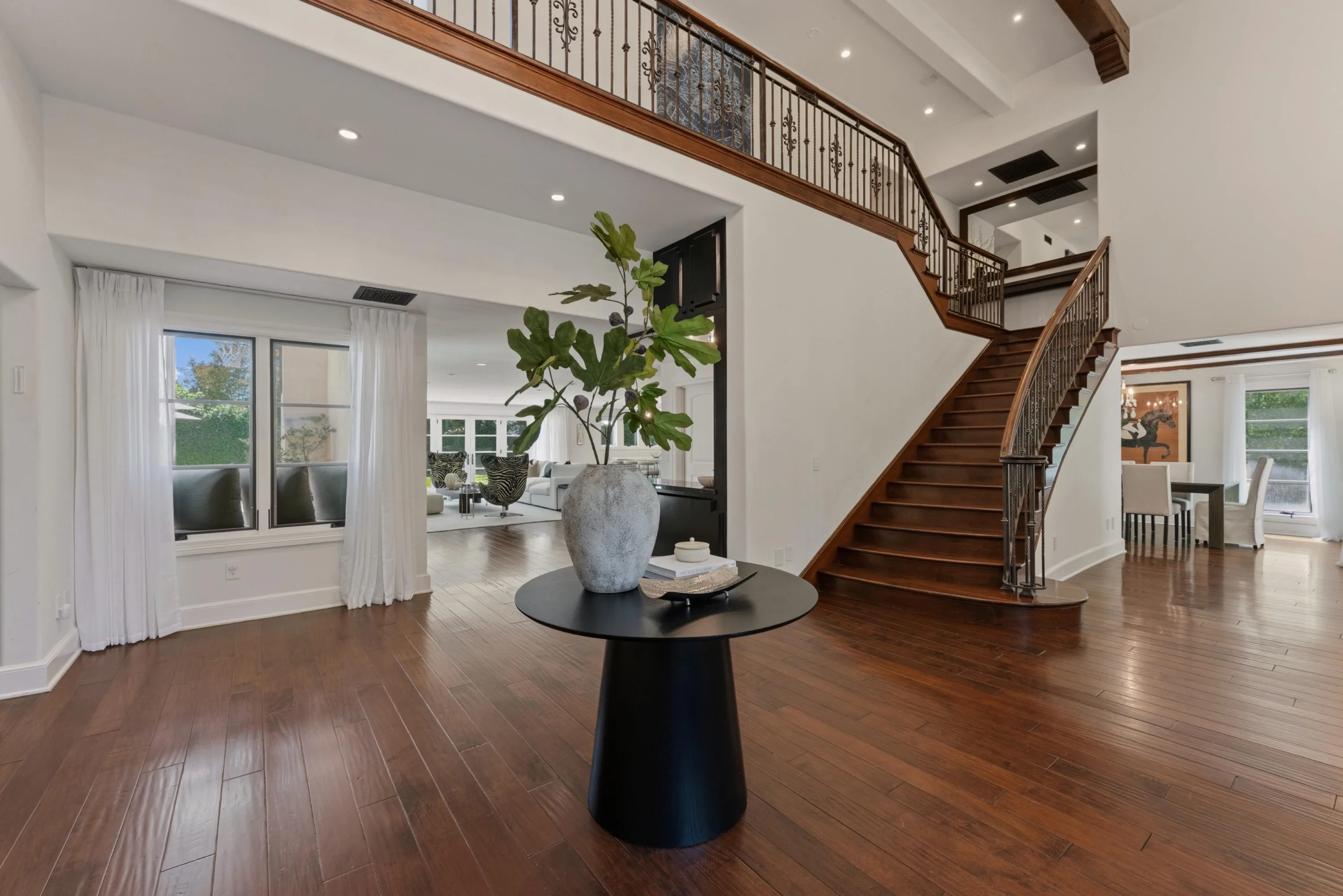 Double-height foyer with curved wood staircase, ironwork balustrade and round entry table