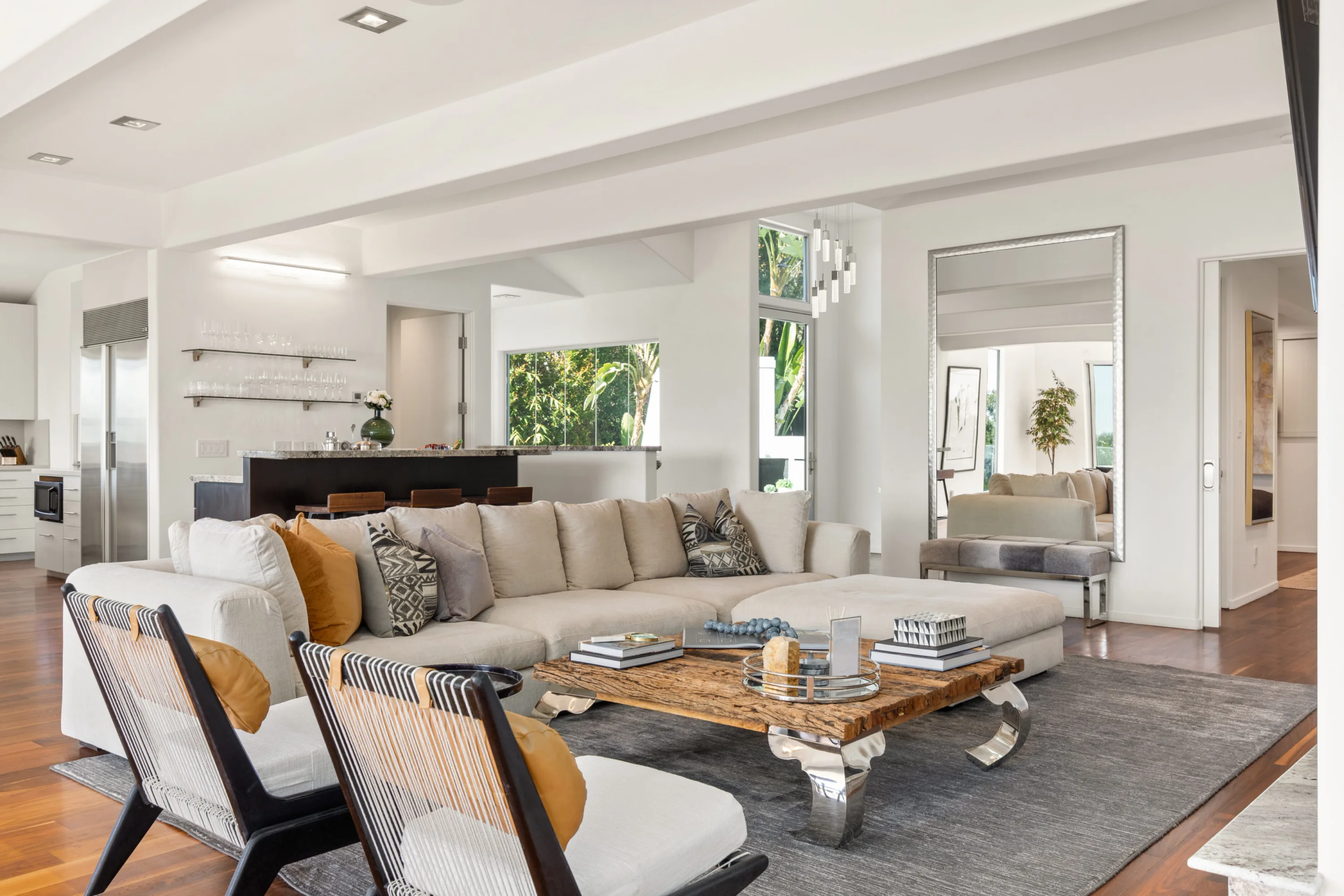 Living room seating grouped around a live-edge coffee table, with bar shelving and kitchen beyond