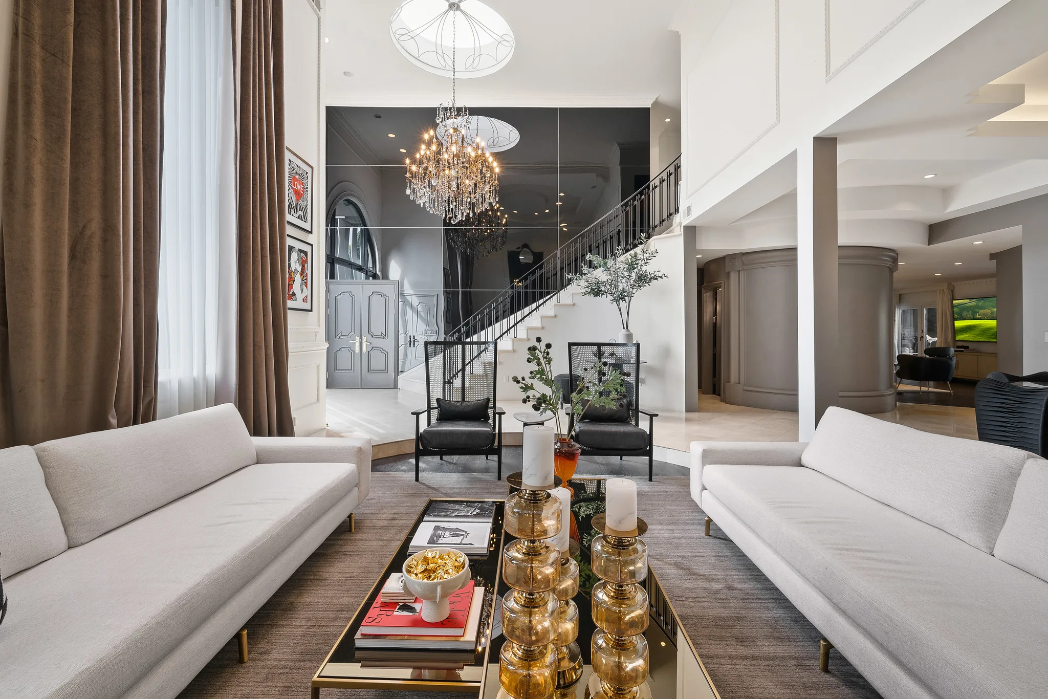 View across facing sofas toward the mirrored entry hall and curved white staircase