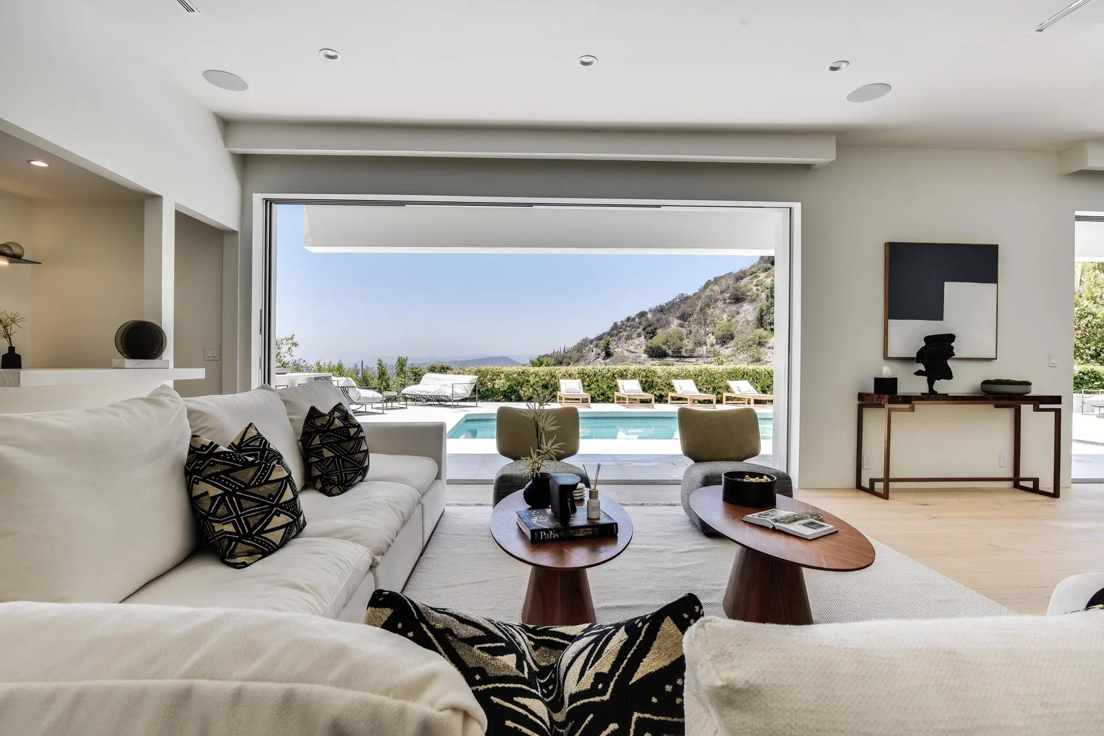 Second lounge with cream sectionals framing an open-air view of the pool and chaparral hillside