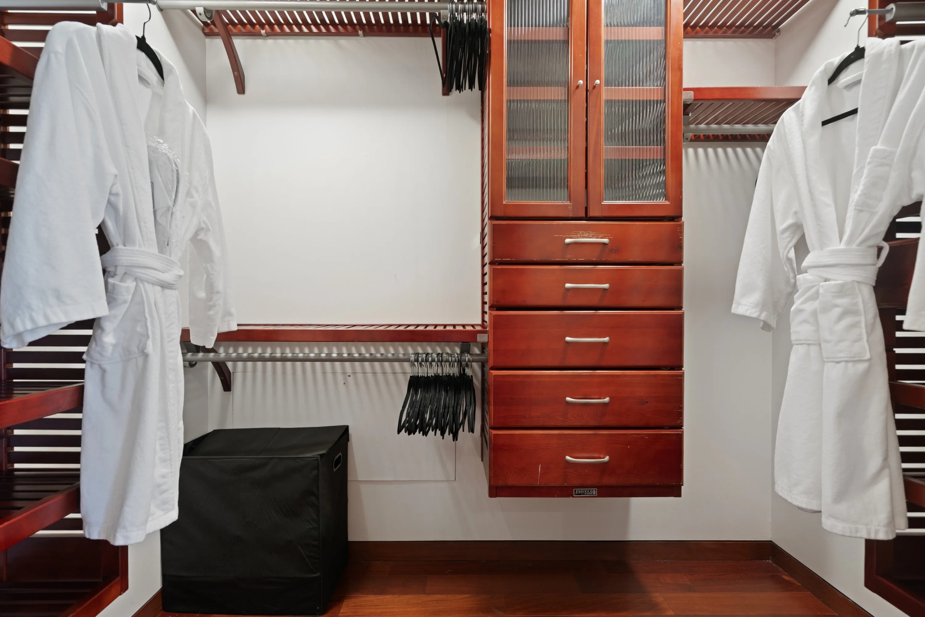 Walk-in dressing room in cherry cabinetry with white robes hung ready on either side