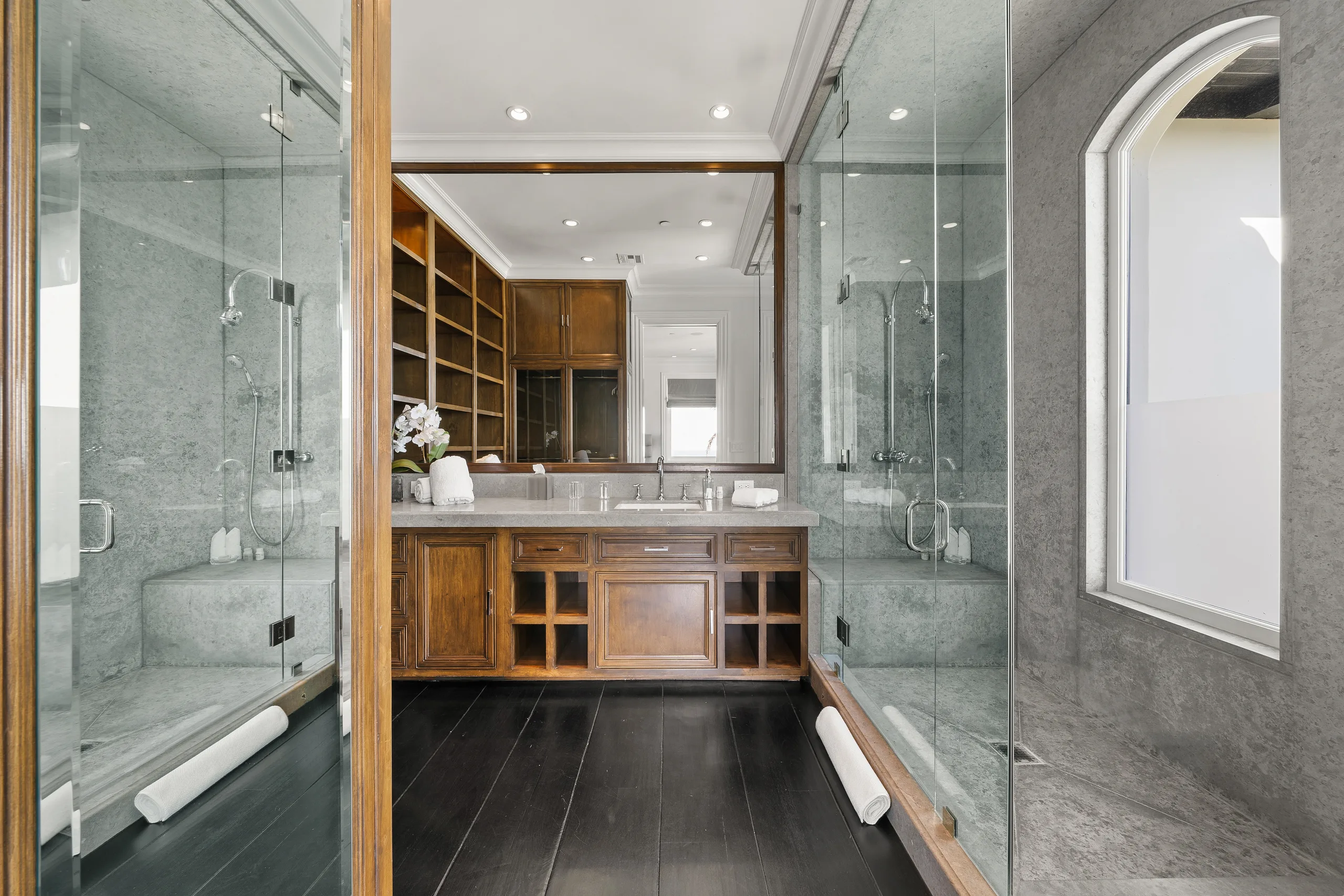Twin glass shower enclosures flanking a timber vanity in a stone-clad ensuite