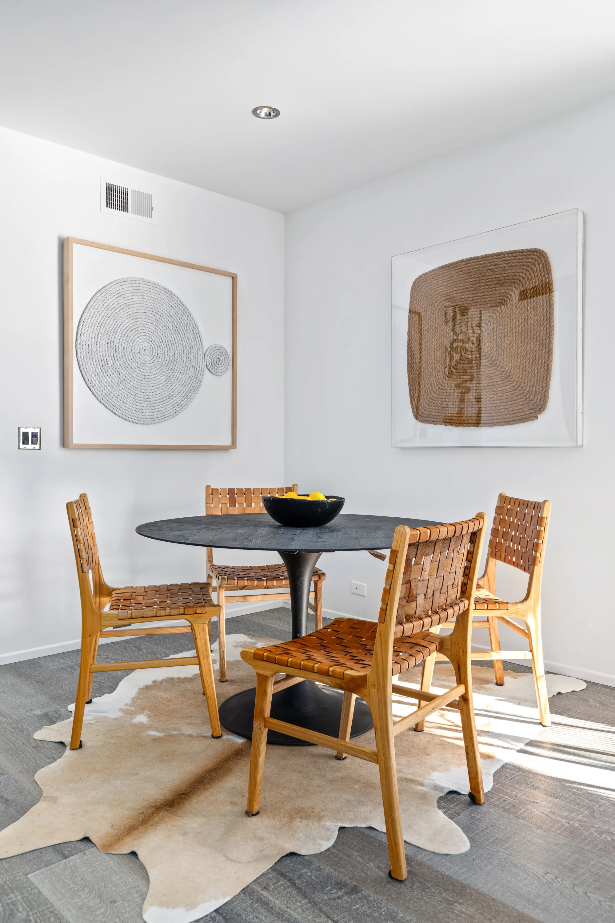 Breakfast nook with round black table, woven leather chairs and framed fibre artworks