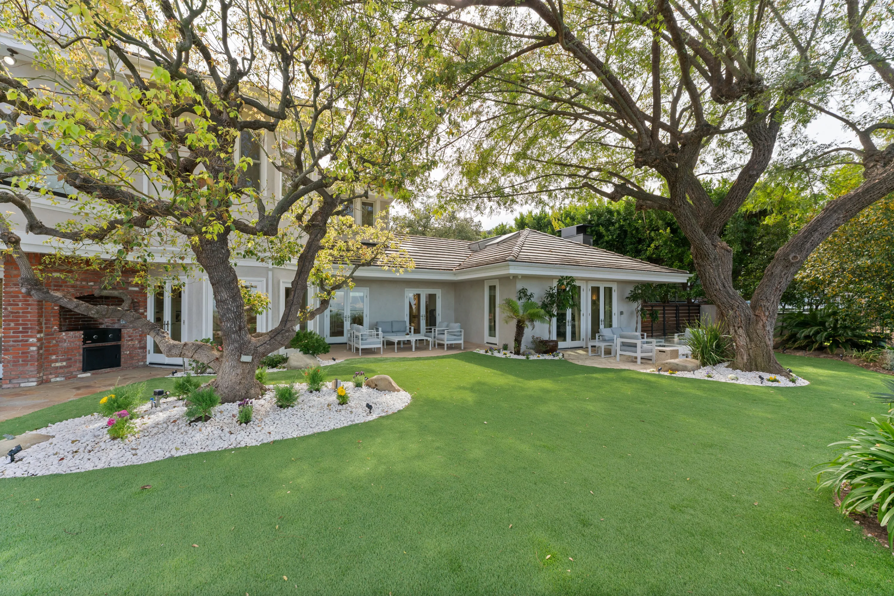 Park-like Brentwood lawn shaded by mature trees, with a covered patio lounge and built-in barbecue