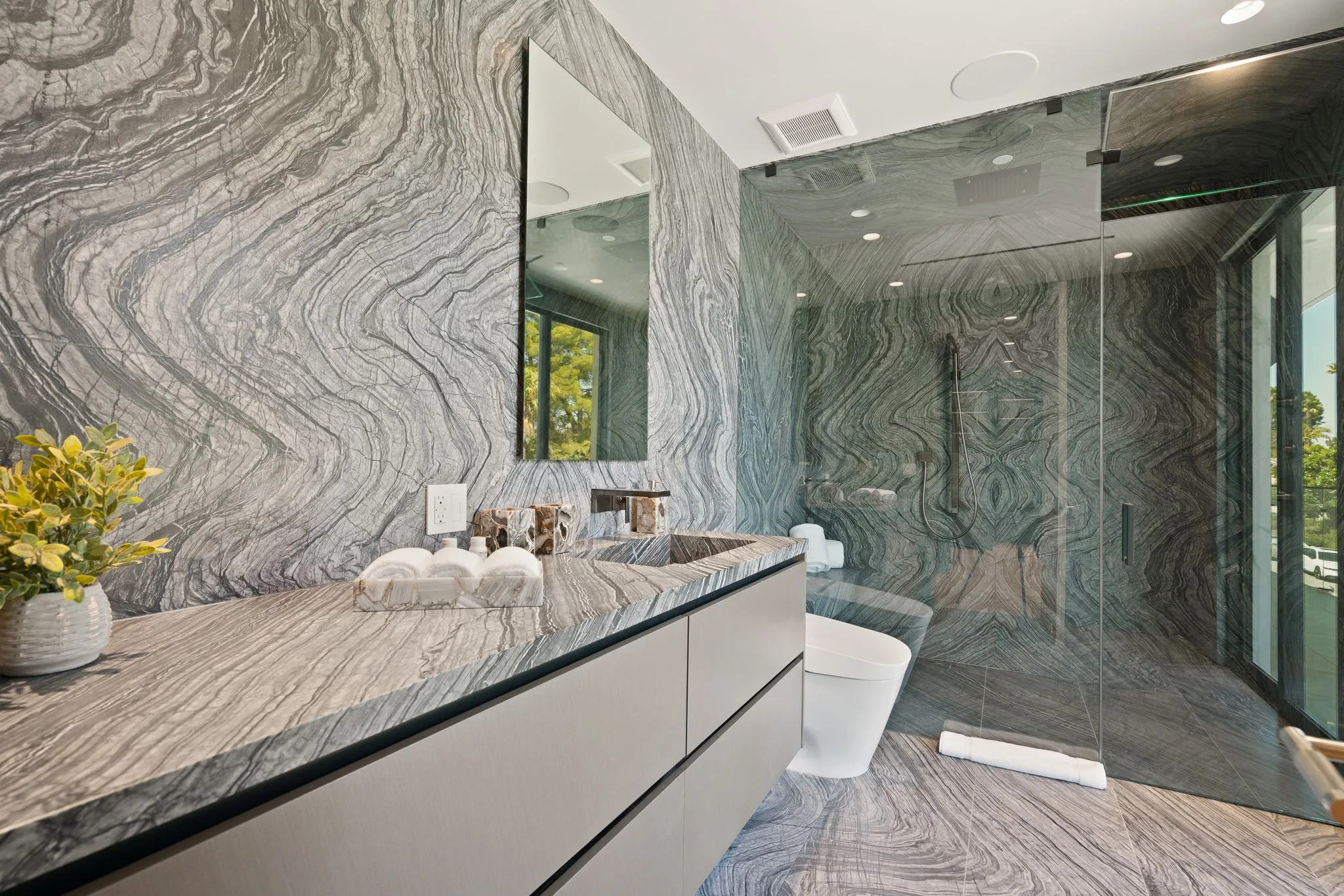 Primary bathroom wrapped in dramatically veined grey marble, with floating vanity and glass rain shower
