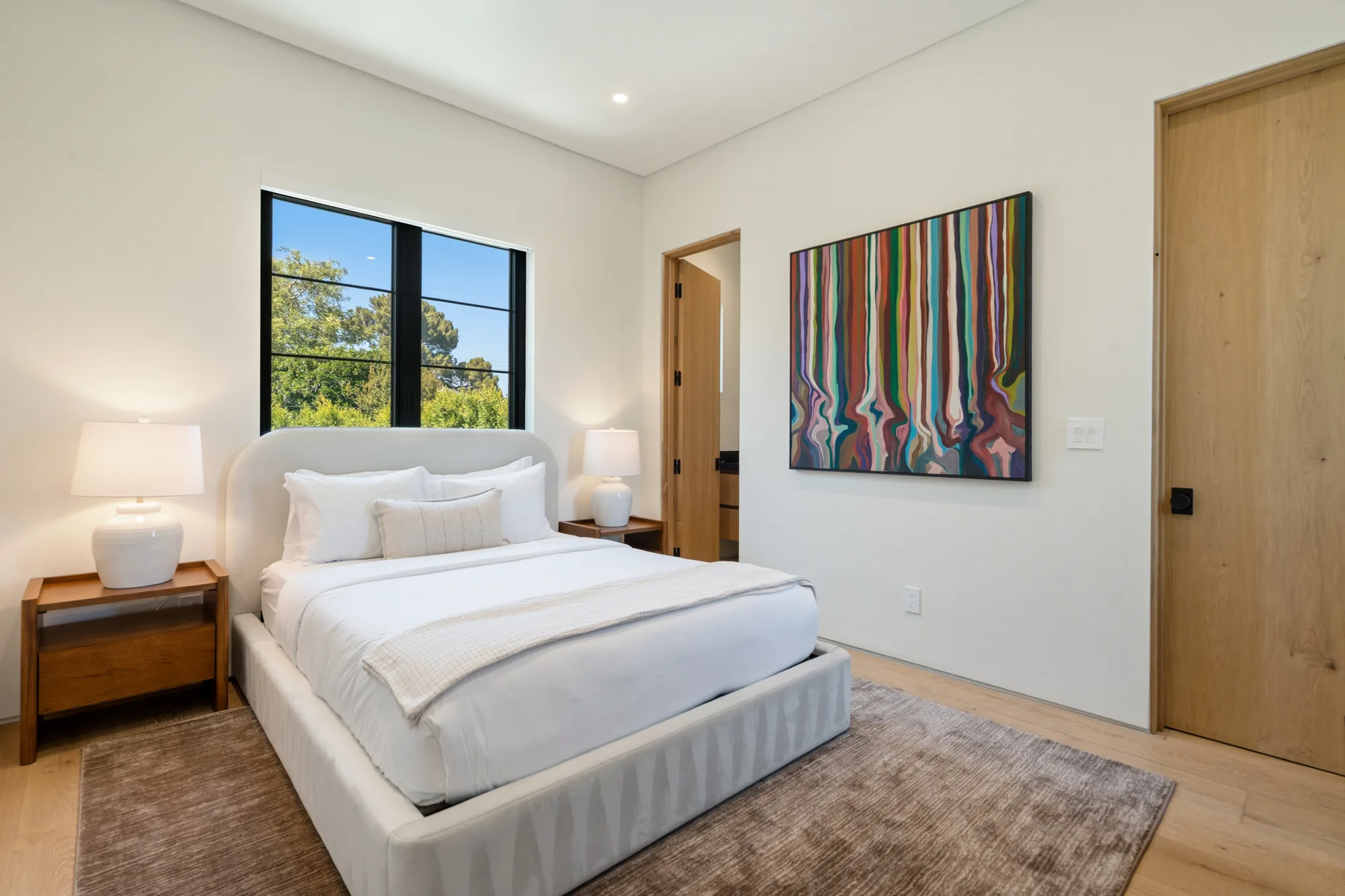Guest bedroom with curved upholstered headboard, striped colour-field artwork and ensuite doorway