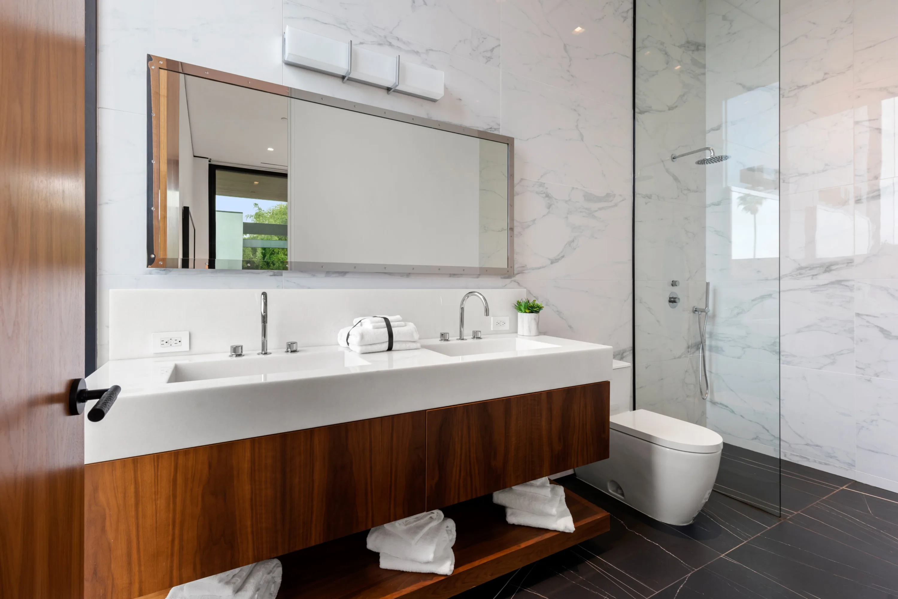 Marble-clad guest bath with double trough vanity, walnut floating cabinet and glass walk-in shower