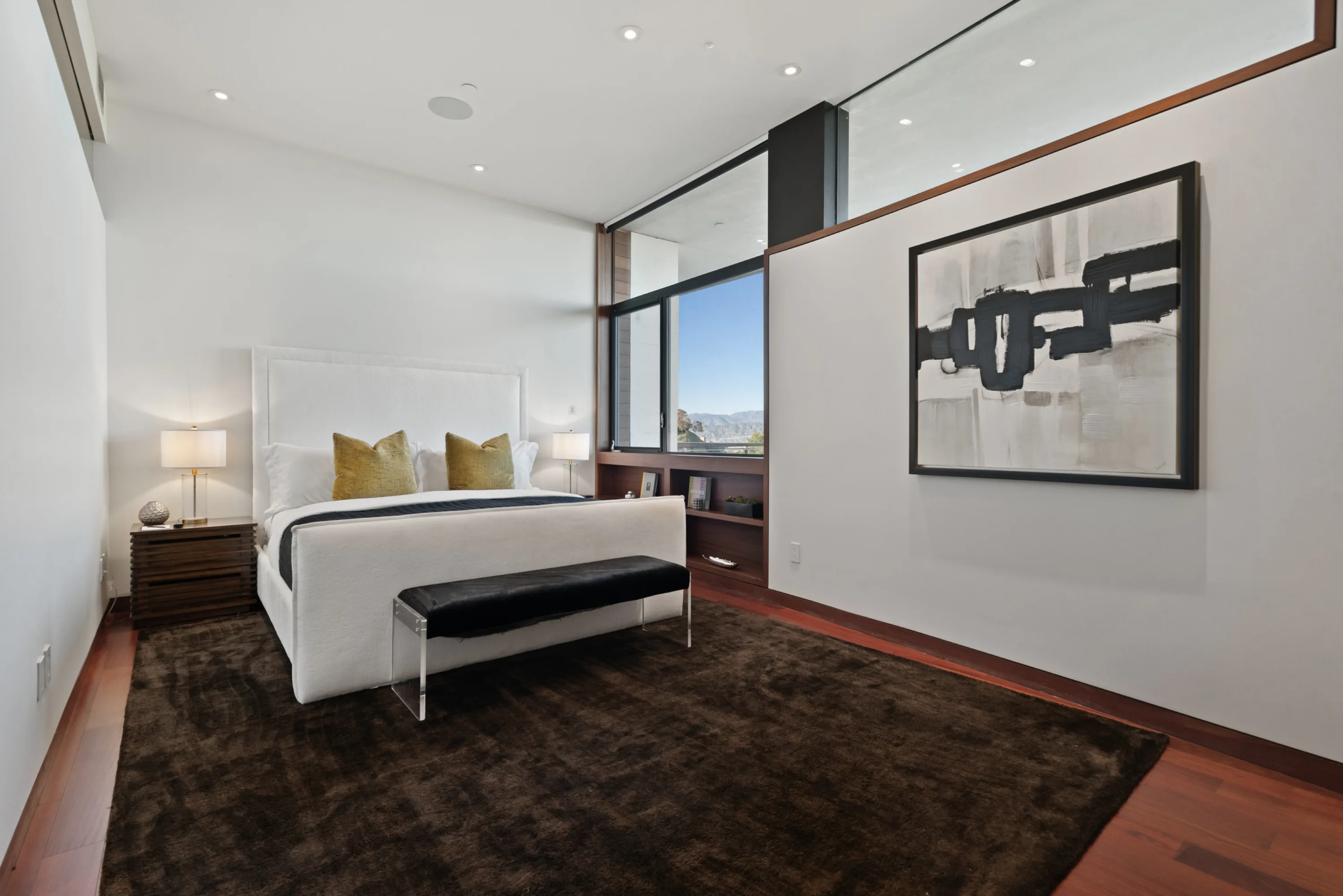 Guest bedroom with upholstered bed, leather bench and corner window framing a hillside view