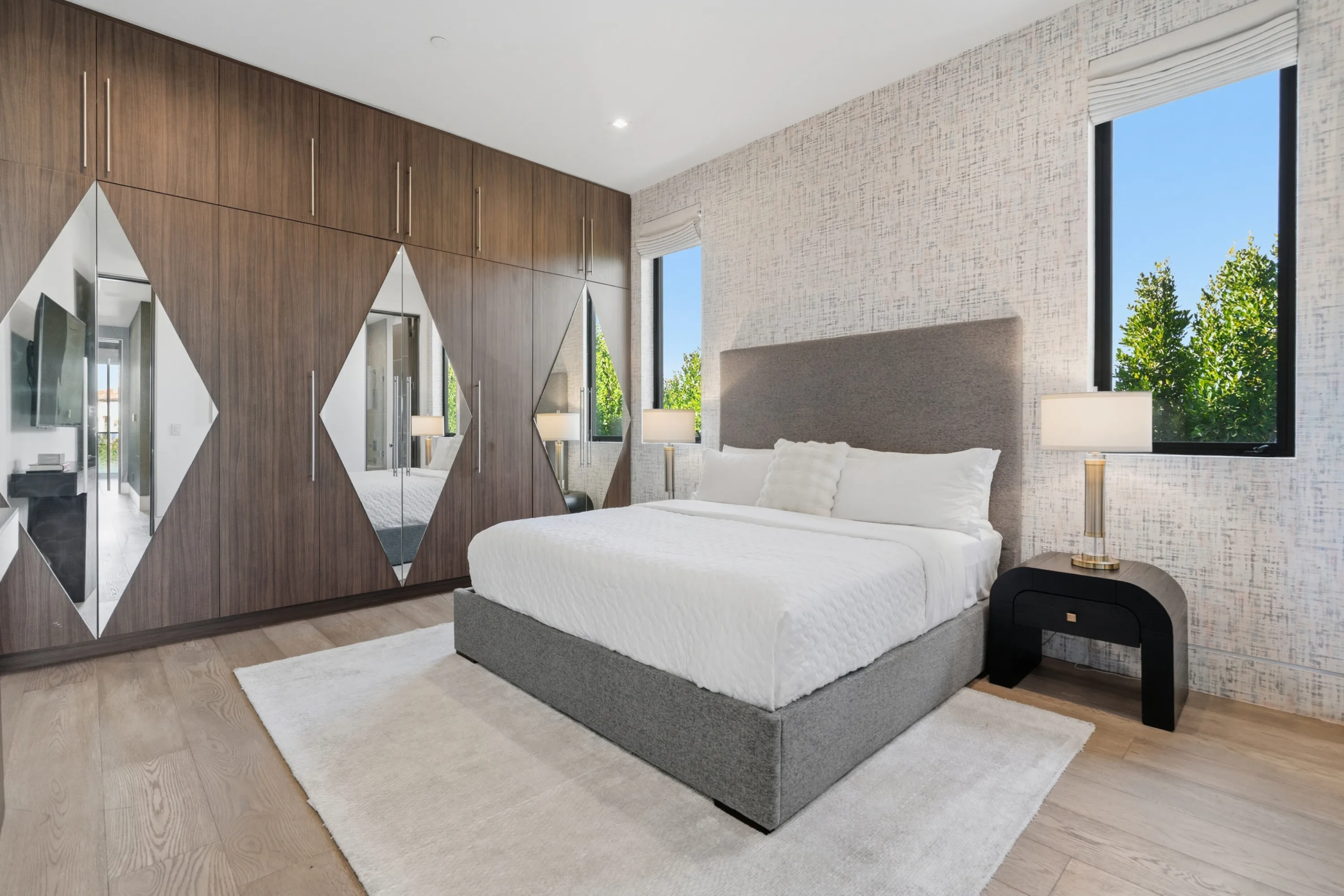 Bedroom with grey upholstered bed, textured wallcovering and mirrored walnut wardrobe wall