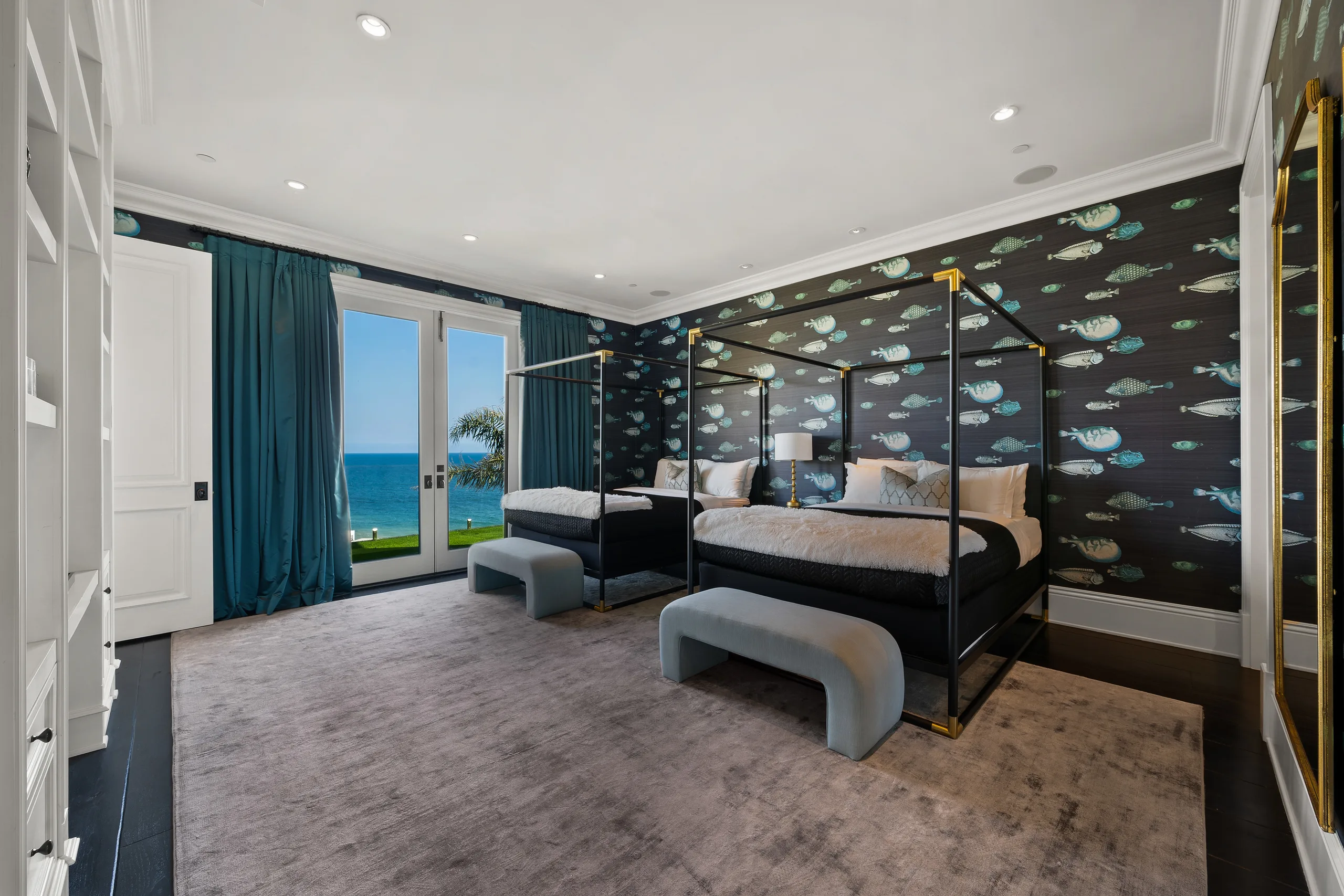 Twin four-poster bedroom with fish-print wallpaper, teal drapes and doors opening to lawn and ocean