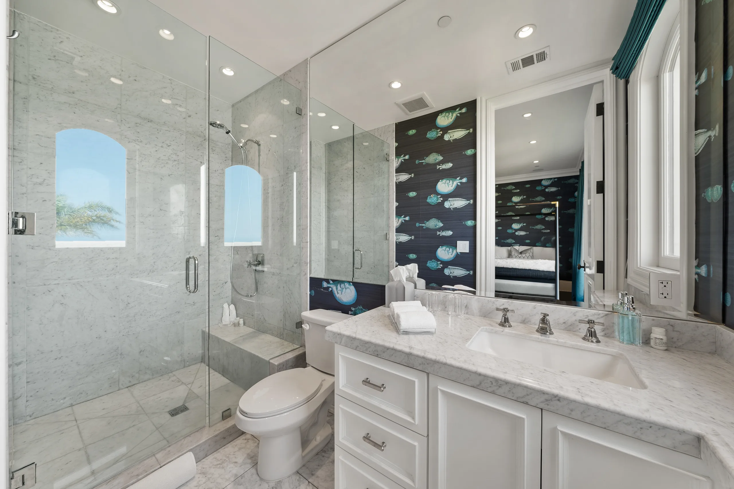 Children's ensuite in white marble, glass shower and arched window, with the fish-papered bedroom reflected