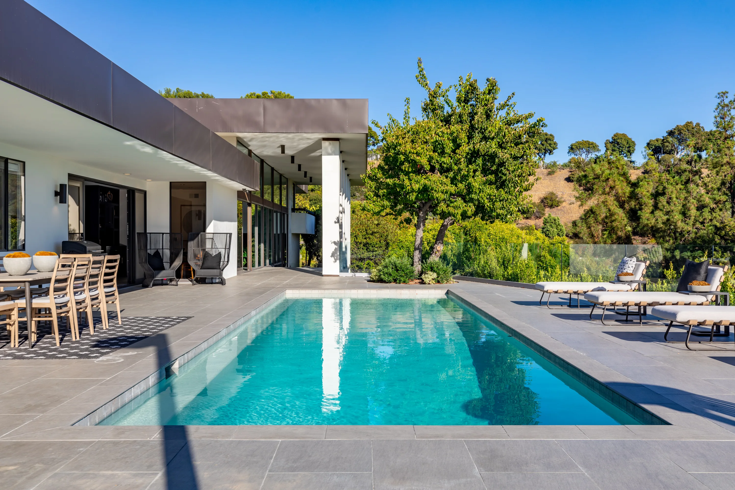 Zero-edge pool bordered by sun loungers, with the low-slung mid-century wing and canyon behind