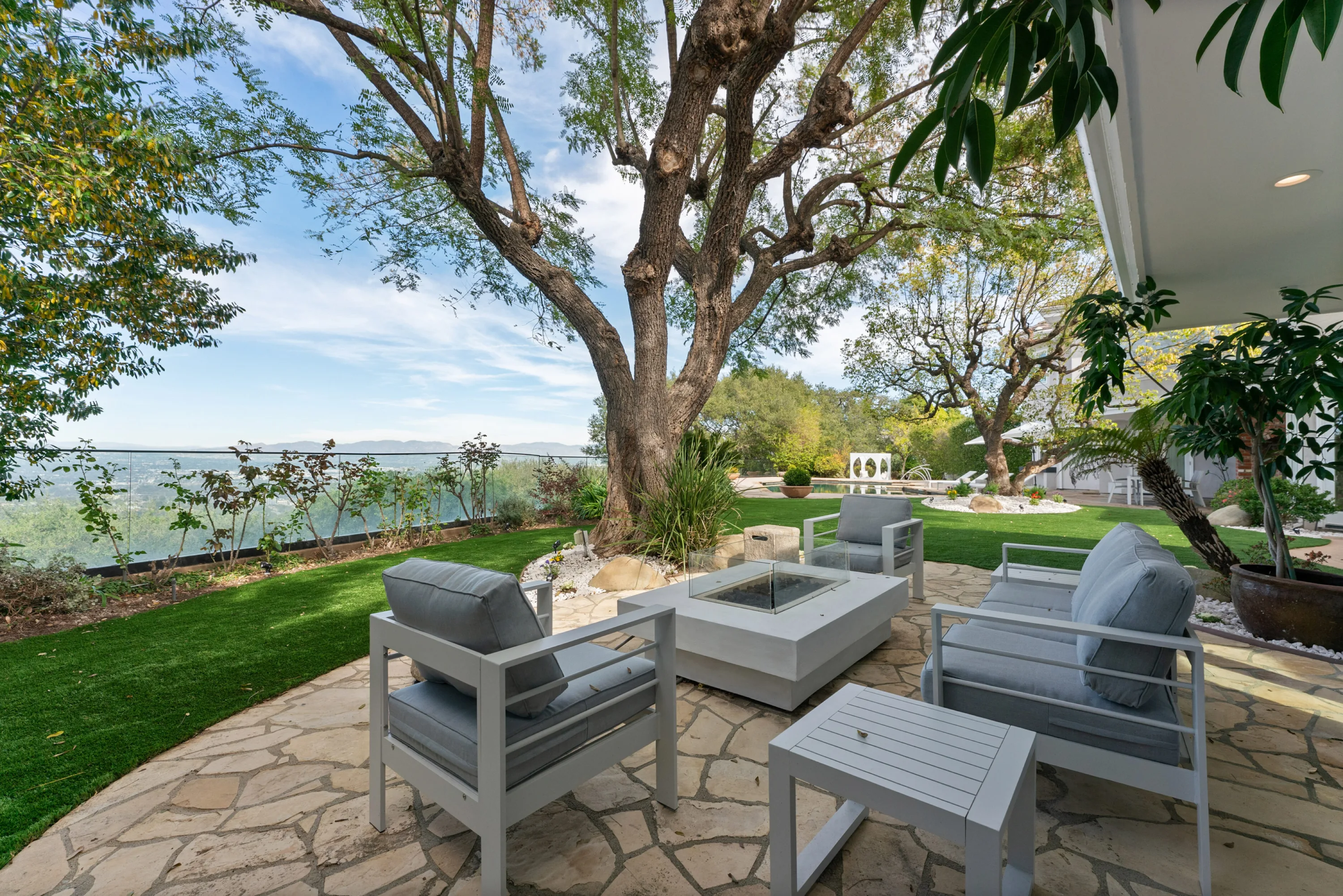 Fire-pit seating on the terrace edge, looking out over a glass-railed hillside to distant mountains
