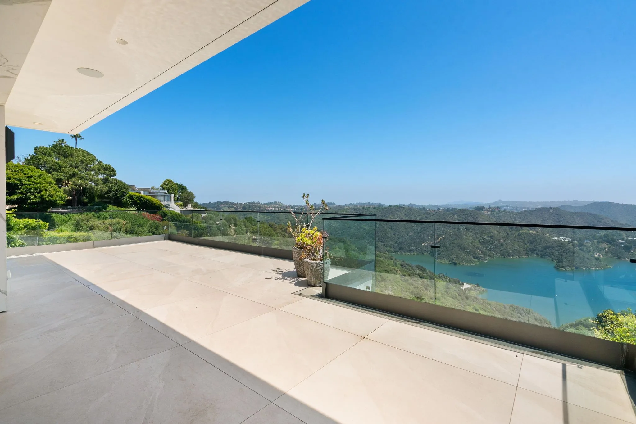 Covered stone terrace with frameless glass railing looking over the Bel Air Reservoir and wooded canyon
