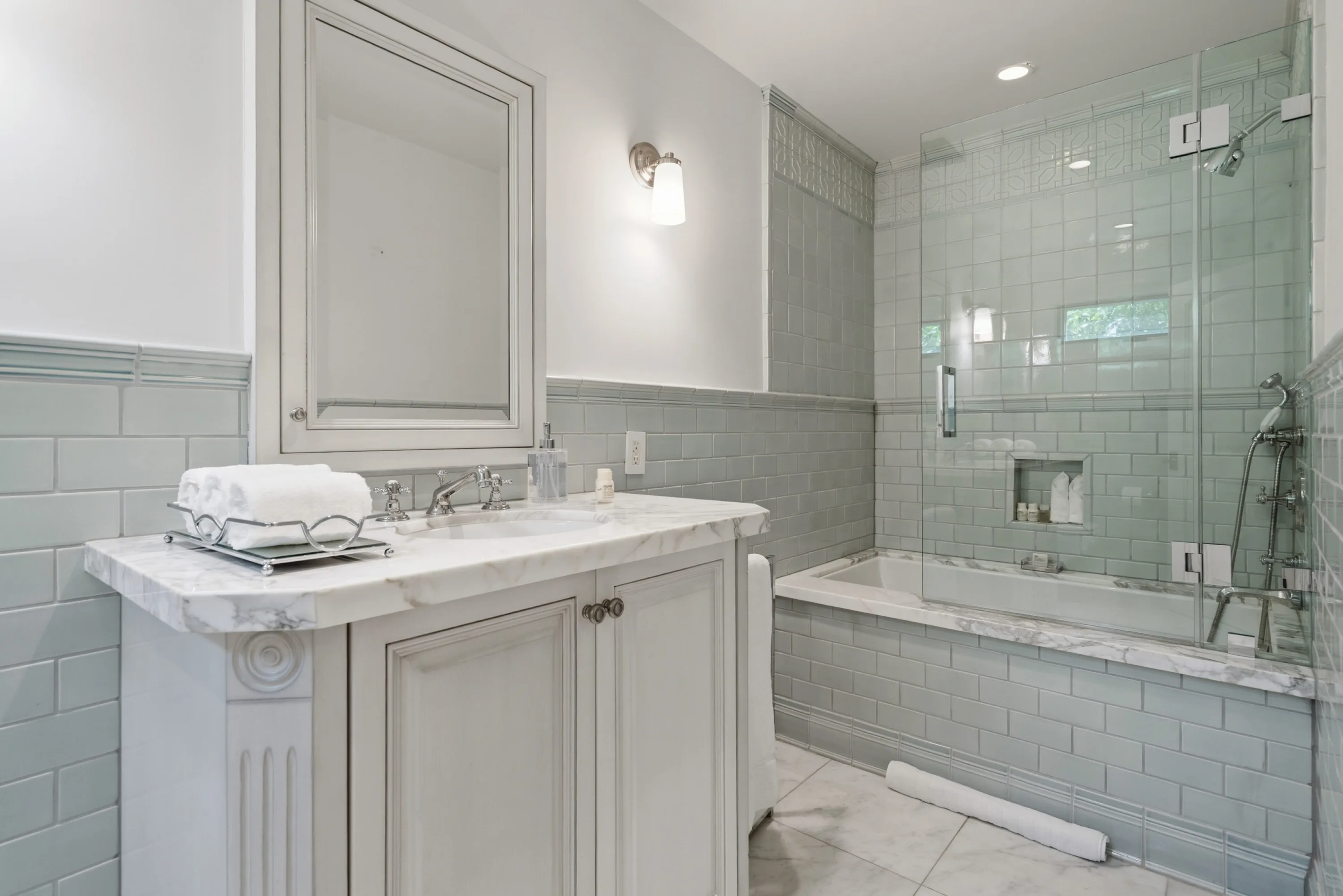 Pale green tiled bath with marble vanity and glass-screened tub-shower