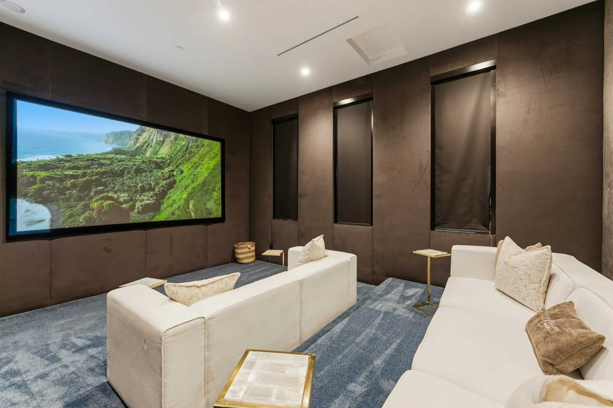 Home cinema in suede-panelled walls, projection screen showing a coastline, two tiers of white sofas