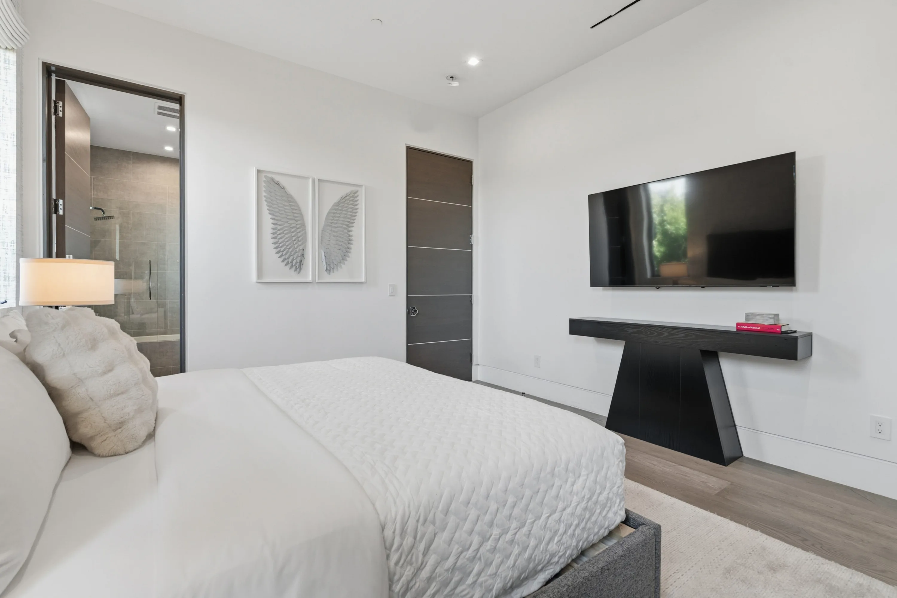 Bedroom with wall-mounted screen, black cantilevered console and en suite shower visible through the doorway