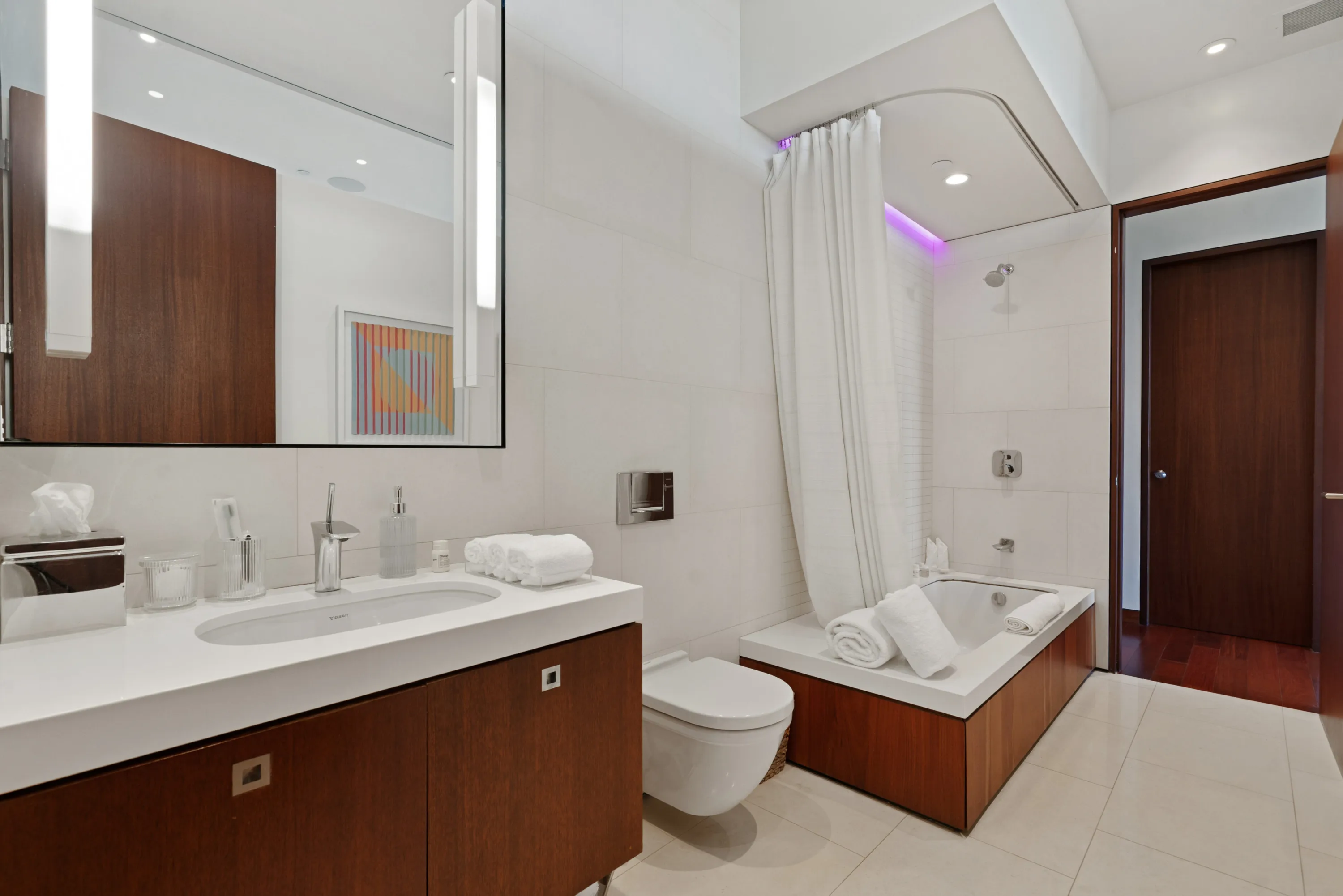 En-suite bathroom with walnut vanity, soaking tub and violet cove lighting above the shower