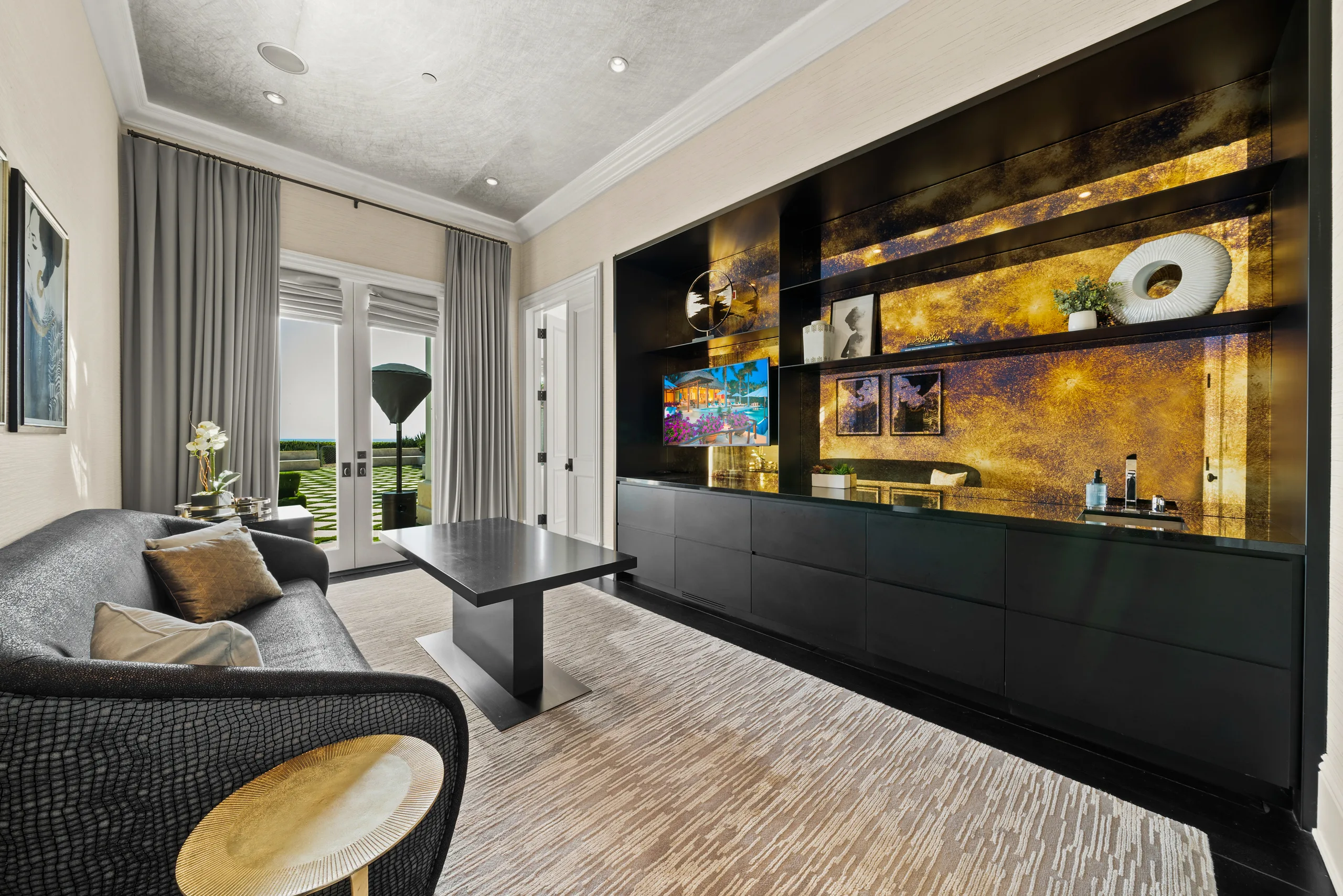 Lounge and bar room with backlit gilded shelving, black cabinetry and garden doors to the pool terrace