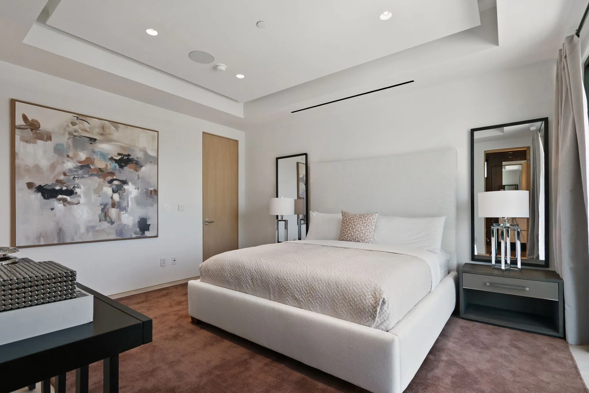 Carpeted guest bedroom with upholstered king bed, large abstract canvas and mirrored bedside niches