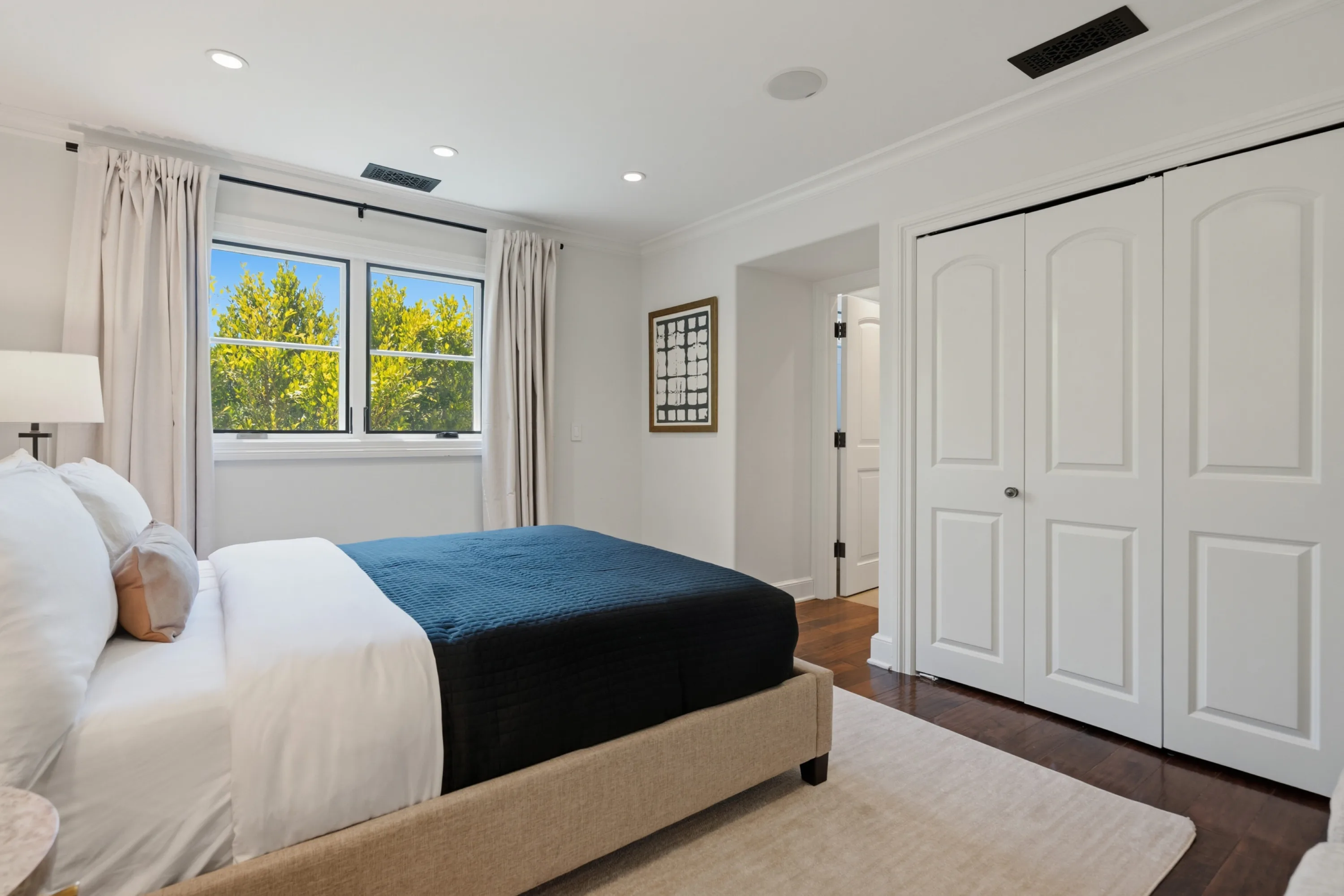 Bright guest room with navy blanket over a linen bed and double closet doors