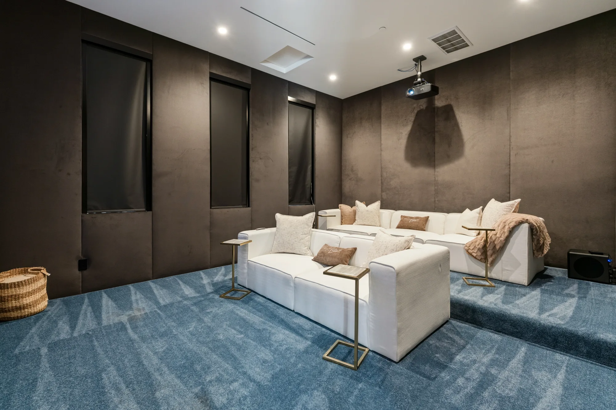 Rear view of the screening room: ceiling projector above a tiered sectional on blue patterned carpet