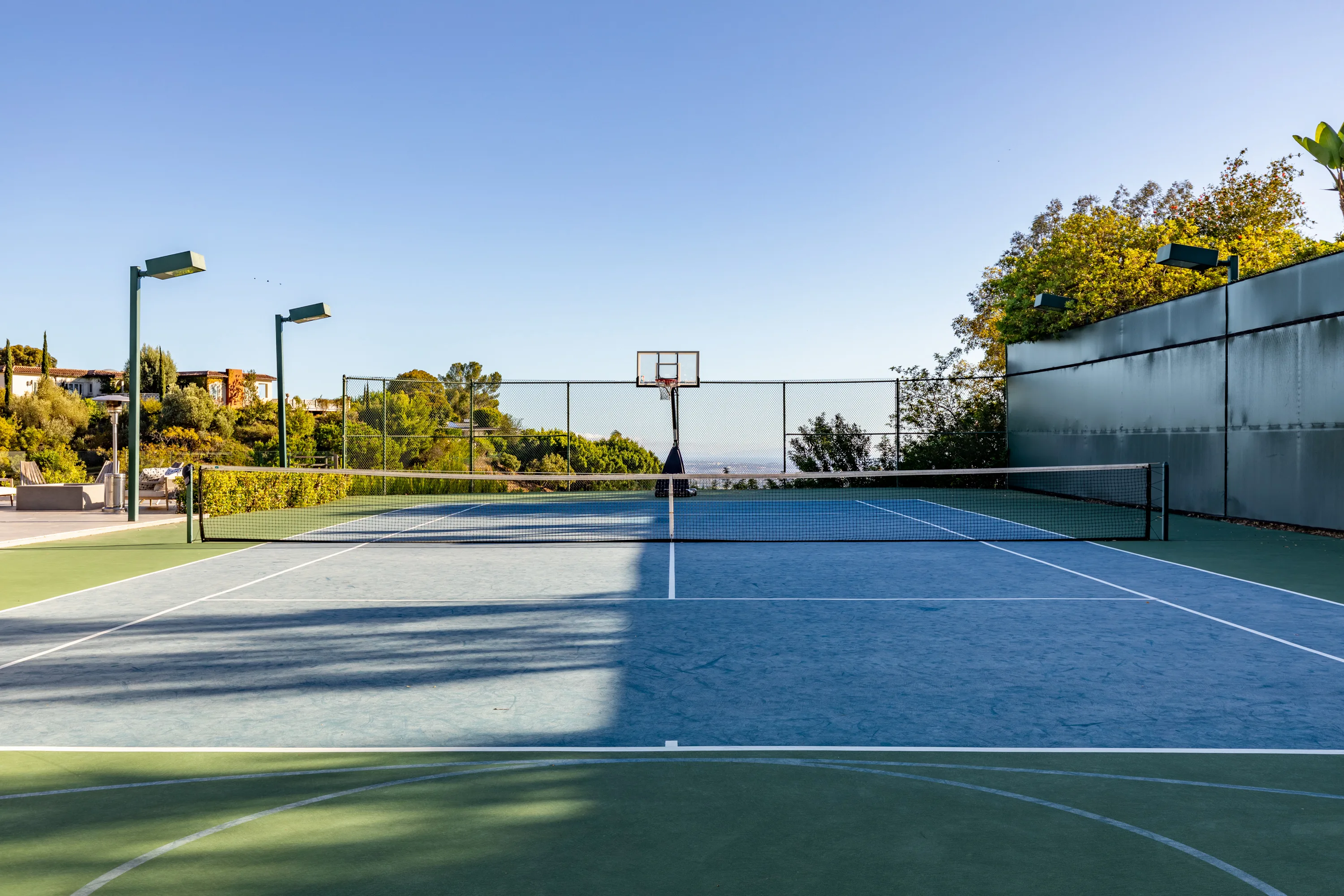 Full-size private tennis court with basketball hoop, court lights and distant city haze