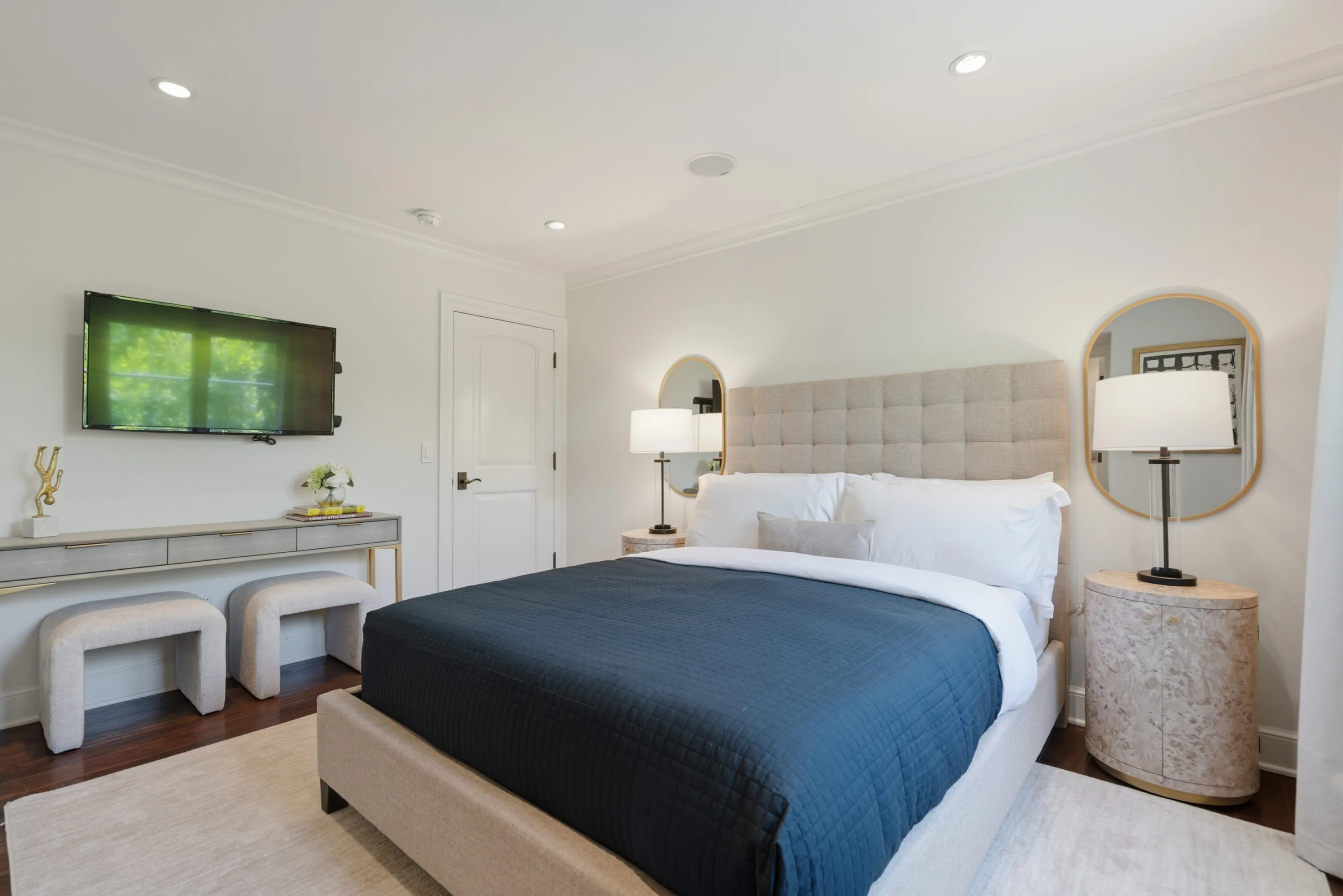 Guest bedroom with tufted headboard, navy coverlet, arched mirrors and a console with paired stools