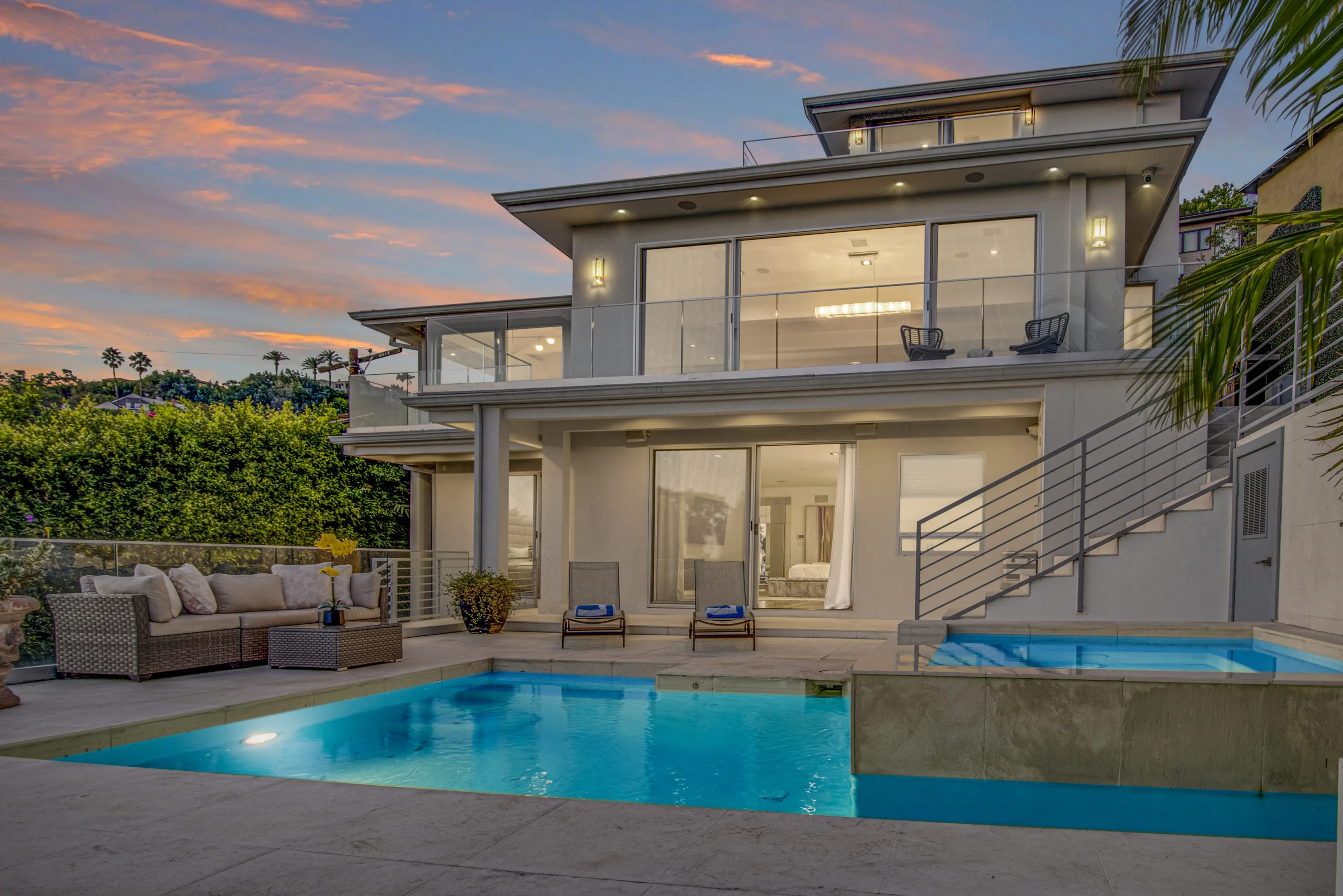 Pool and raised spa at dusk below the lit rear elevation, with sun loungers and a sofa on the deck