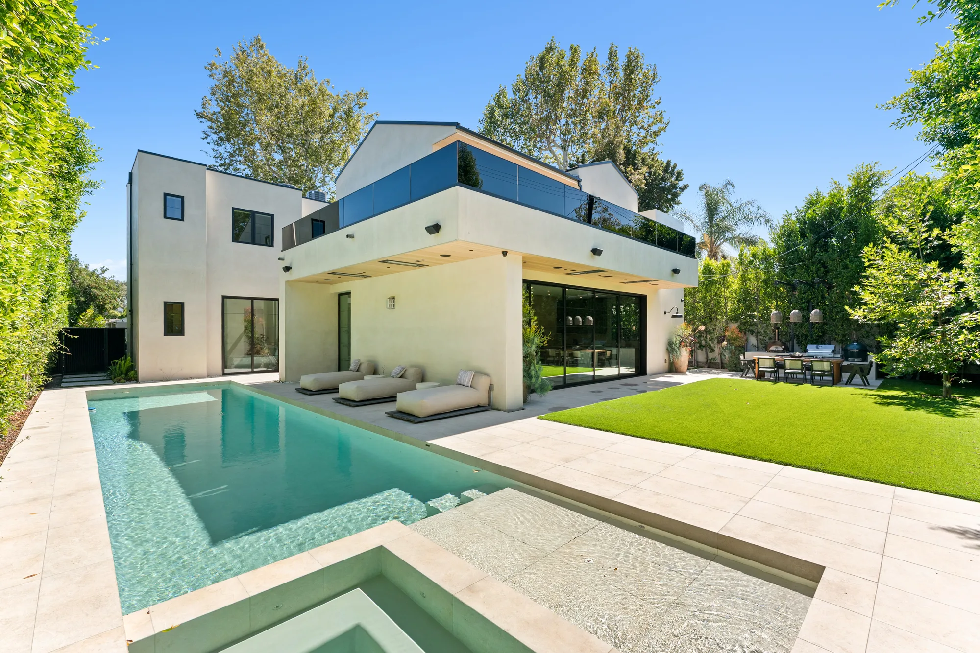Backyard under blue sky with lap pool, sunken spa, shaded loggia, lawn and outdoor kitchen and dining
