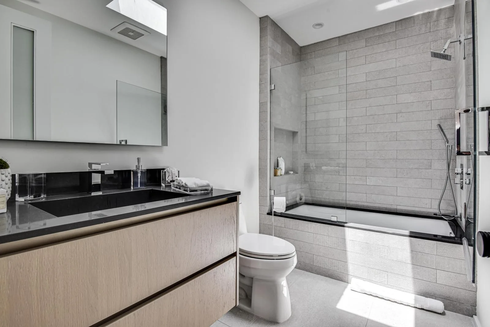 Guest bathroom with oak vanity, black stone top and a soaking tub-shower behind glass under a skylight